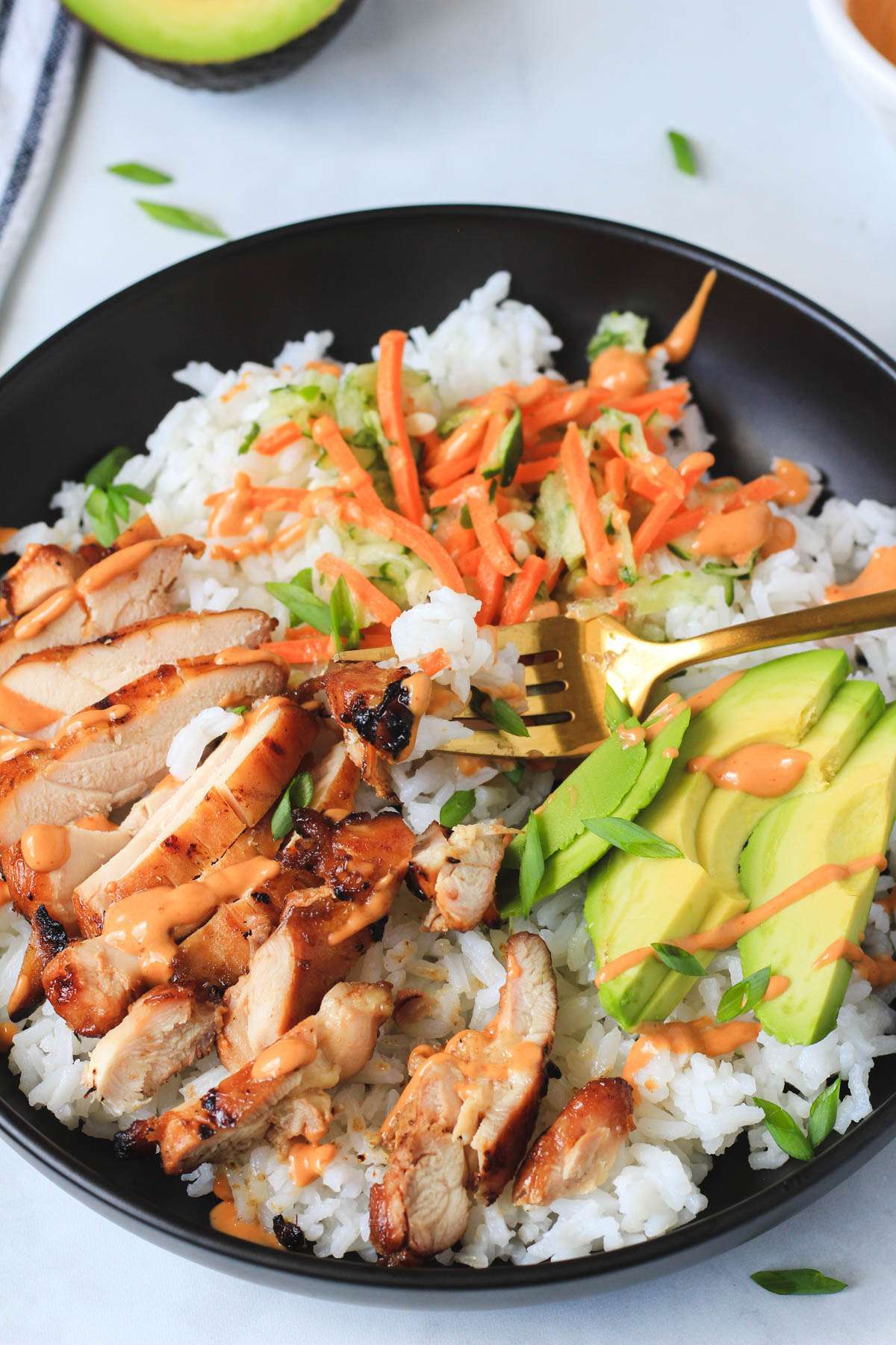 A close up of a gold fork in a soy marinated chicken thigh bowl with chicken and rice on the fork.