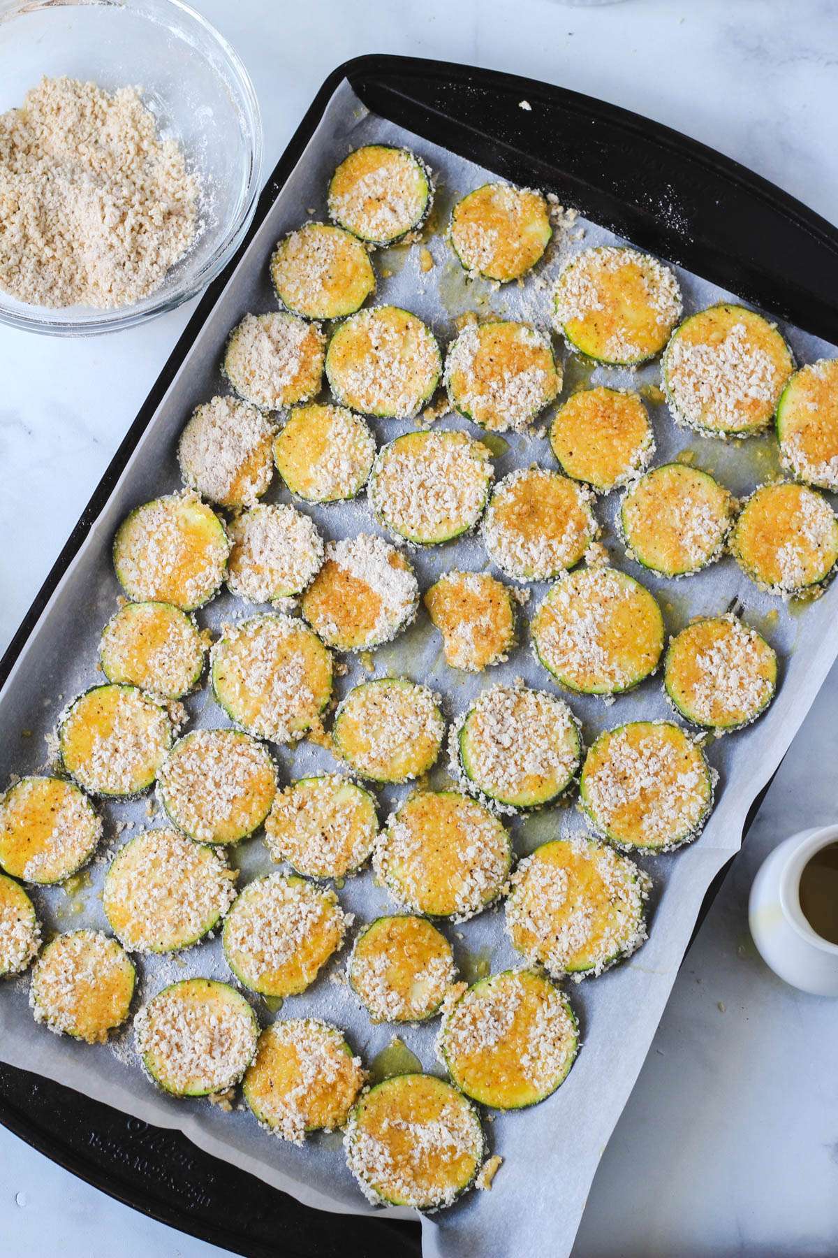 A parchment paper lined baking sheet with spicy zucchini bites drizzled with olive oil.