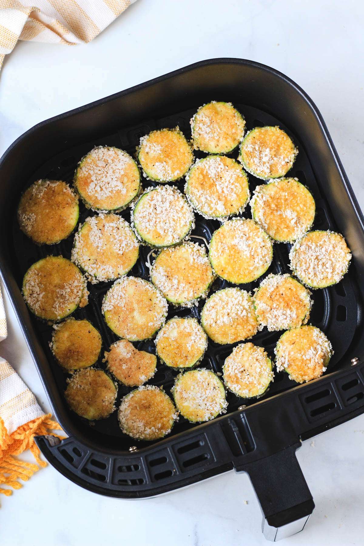 The basket of an air fryer with un baked spicy zucchini bites.