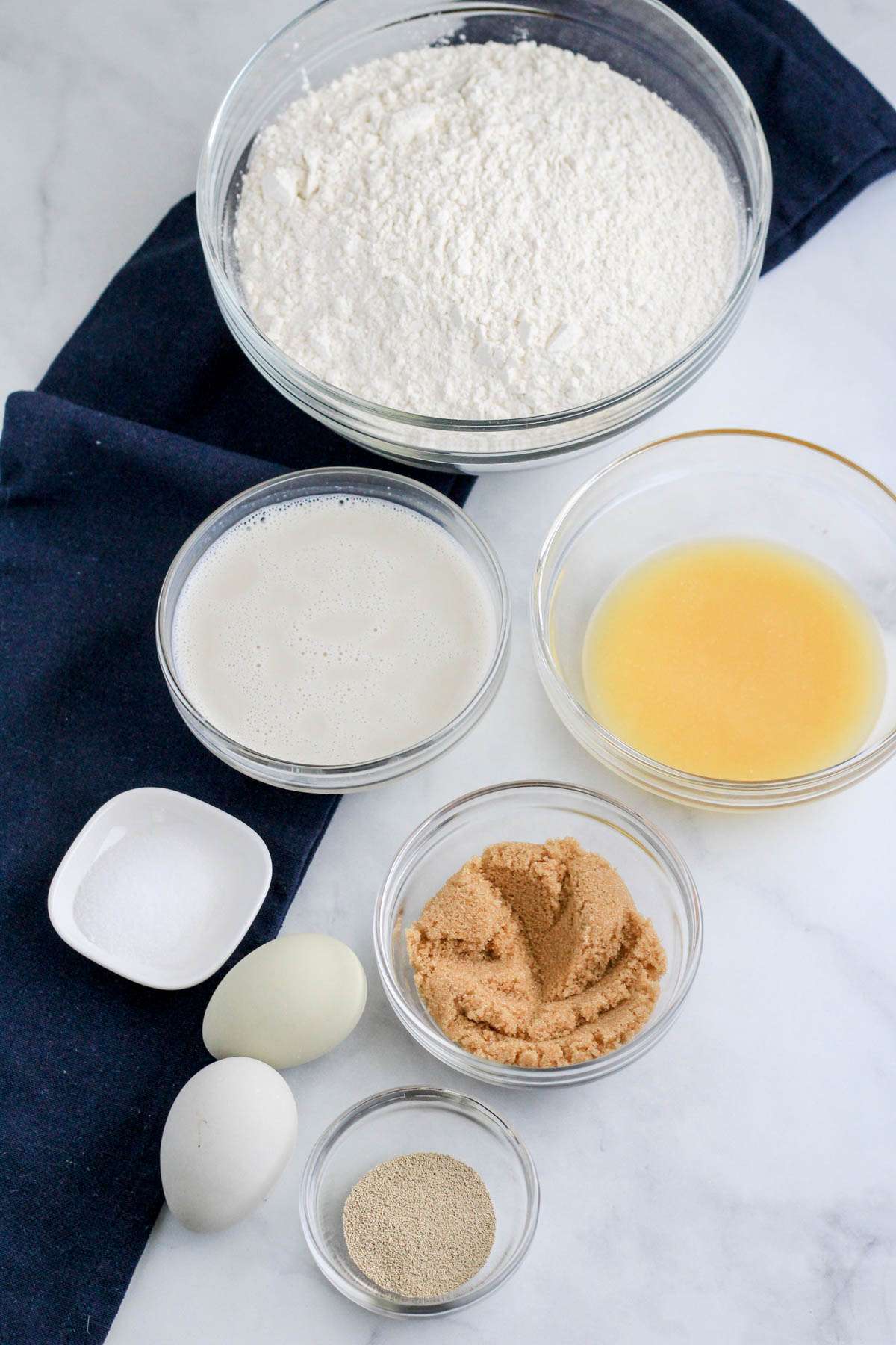Ingredients for cinnamon roll dough on a white counter with a blue dish towel to the left.