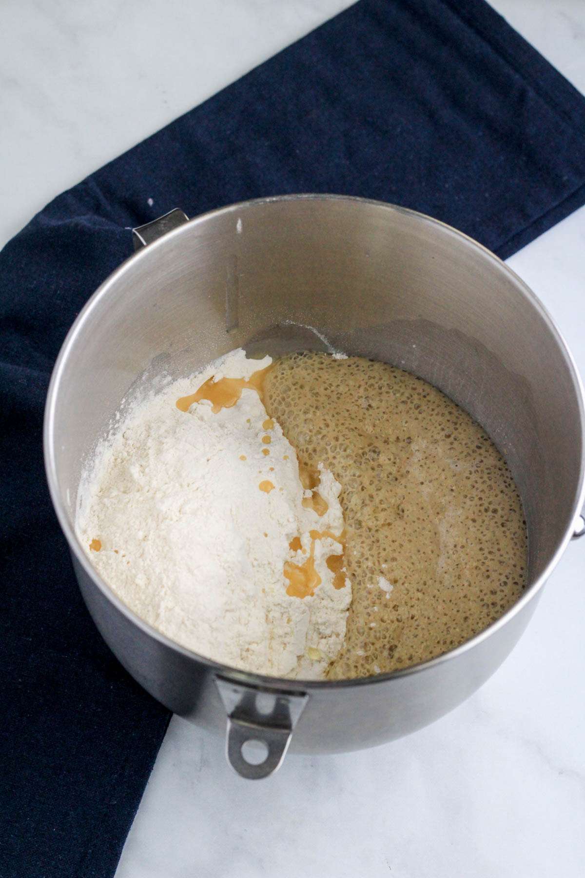 A silver mixing bowl with all of the ingredients for dough before mixing the dough.