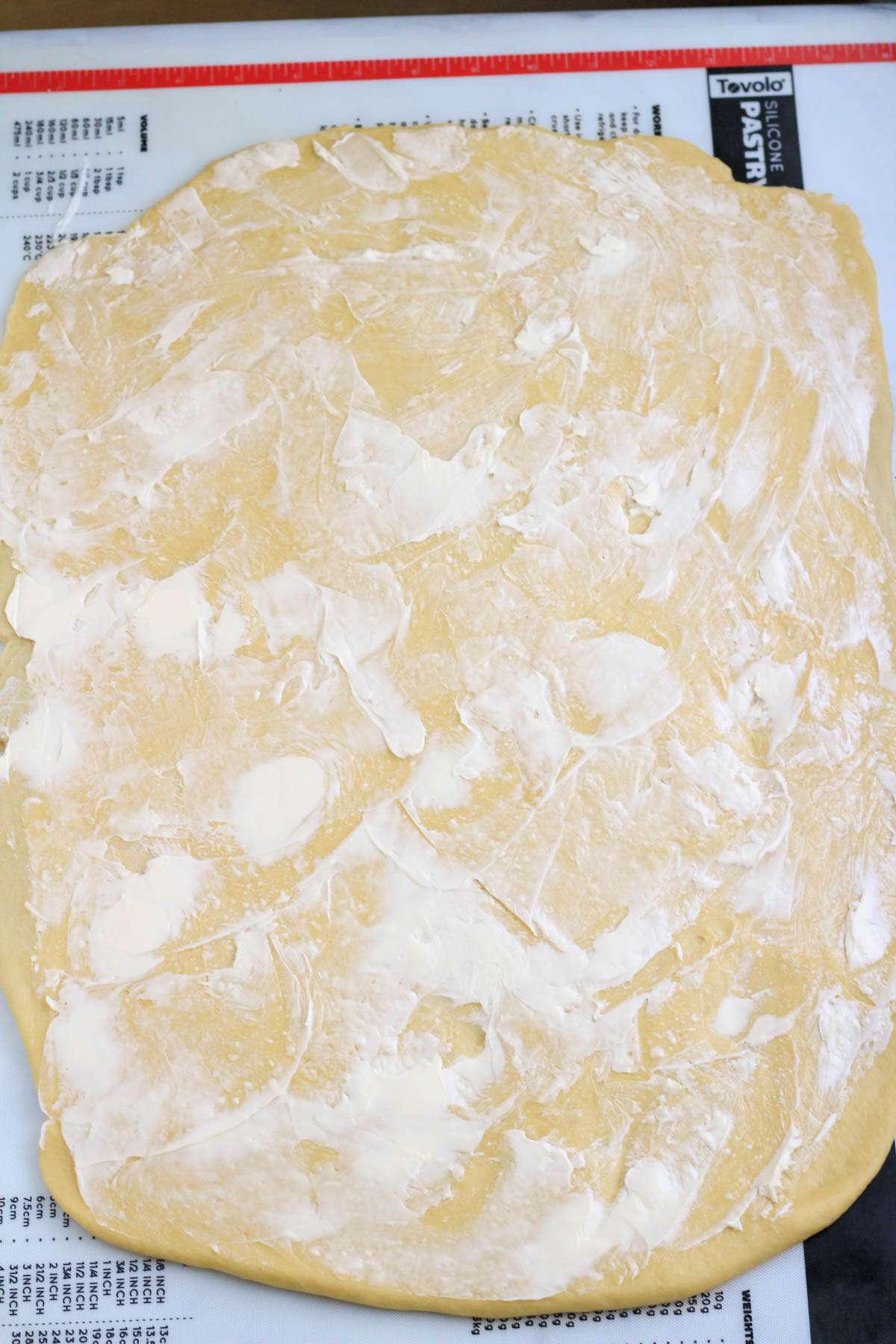 A pastry mat with rolled out cinnamon roll dough with dairy free butter spread out over the dough.
