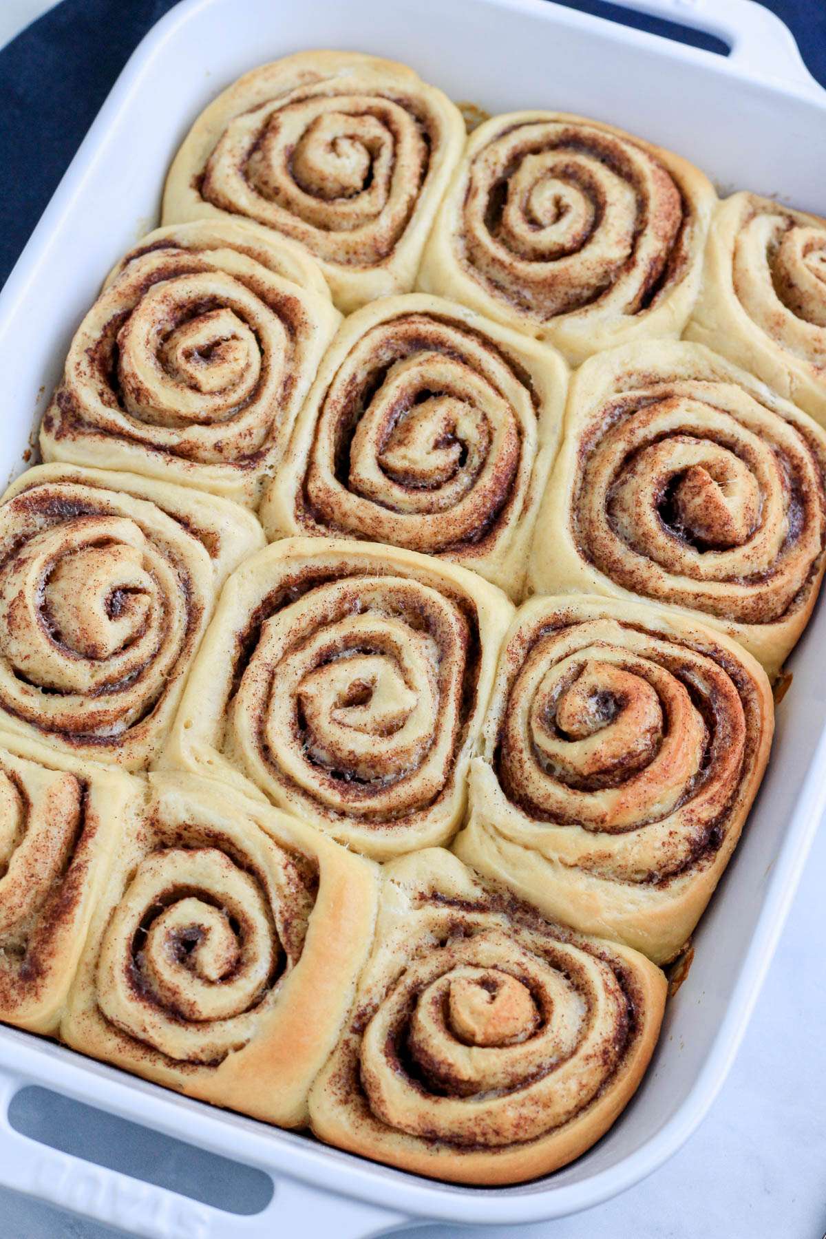Traditional cinnamon rolls after baking before frosting in a white baking pan.