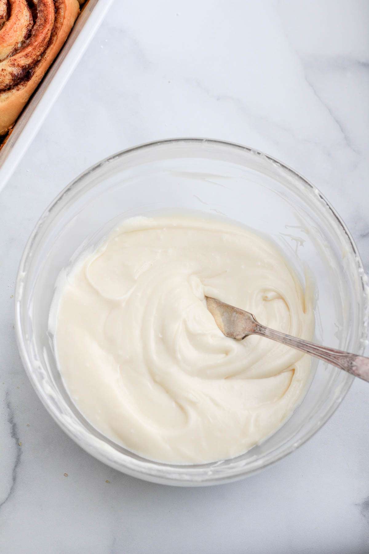 A glass bowl filled with dairy-free cream cheese frosting with a silver knife on the right side of the bowl.