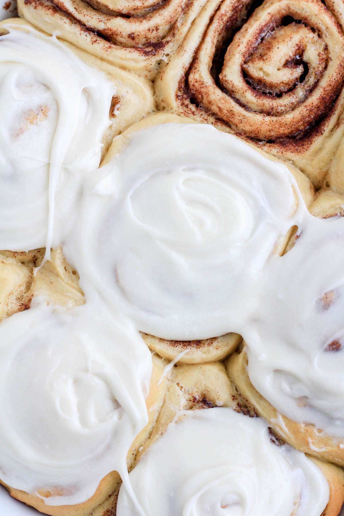 A top down photo of a dairy-free cinnamon roll after being frosted with dairy-free cream cheese frosting.