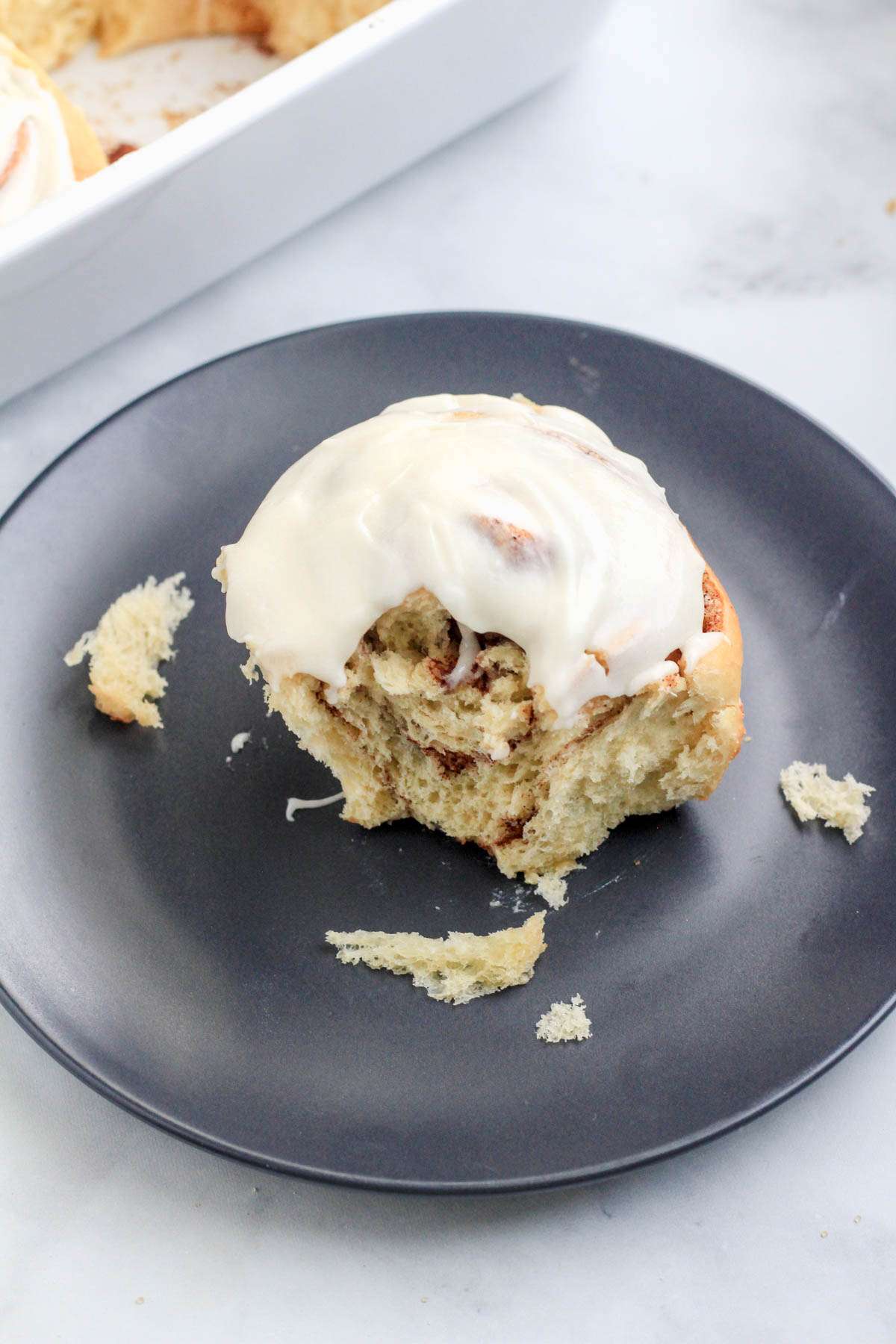 A blue plate with a cinnamon roll missing a bite on a white counter.