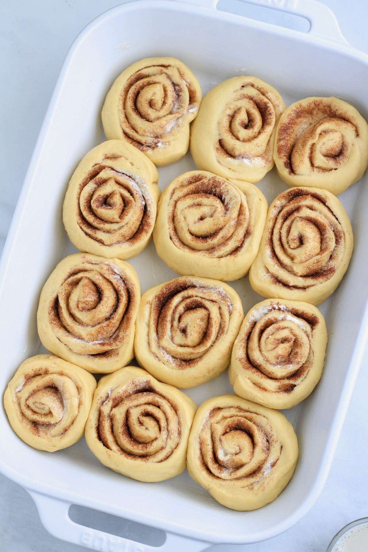 A white baking dish with dairy-free traditional cinnamon rolls before rising for the second time.