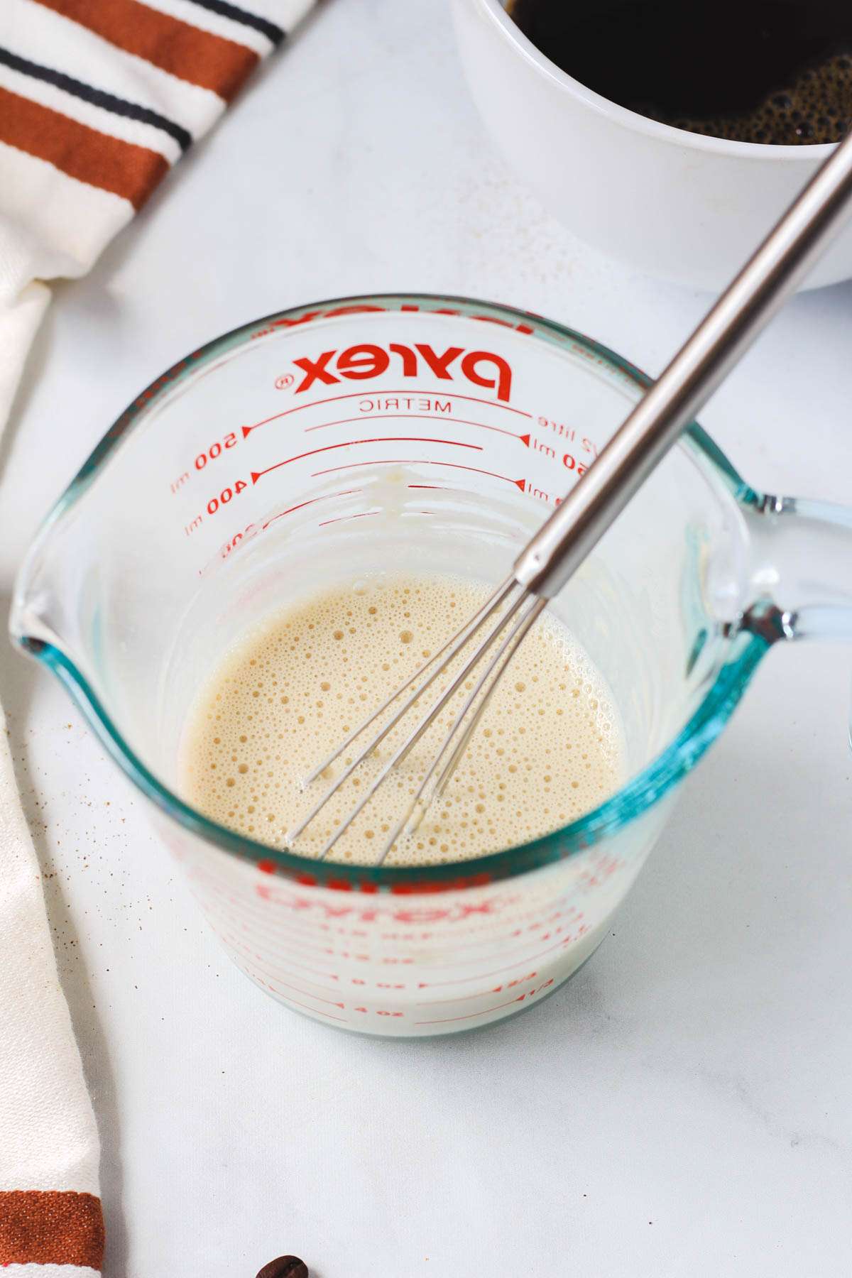 A liquid measuring cup with a small whisk after mixing the vanilla protein into the oat milk.