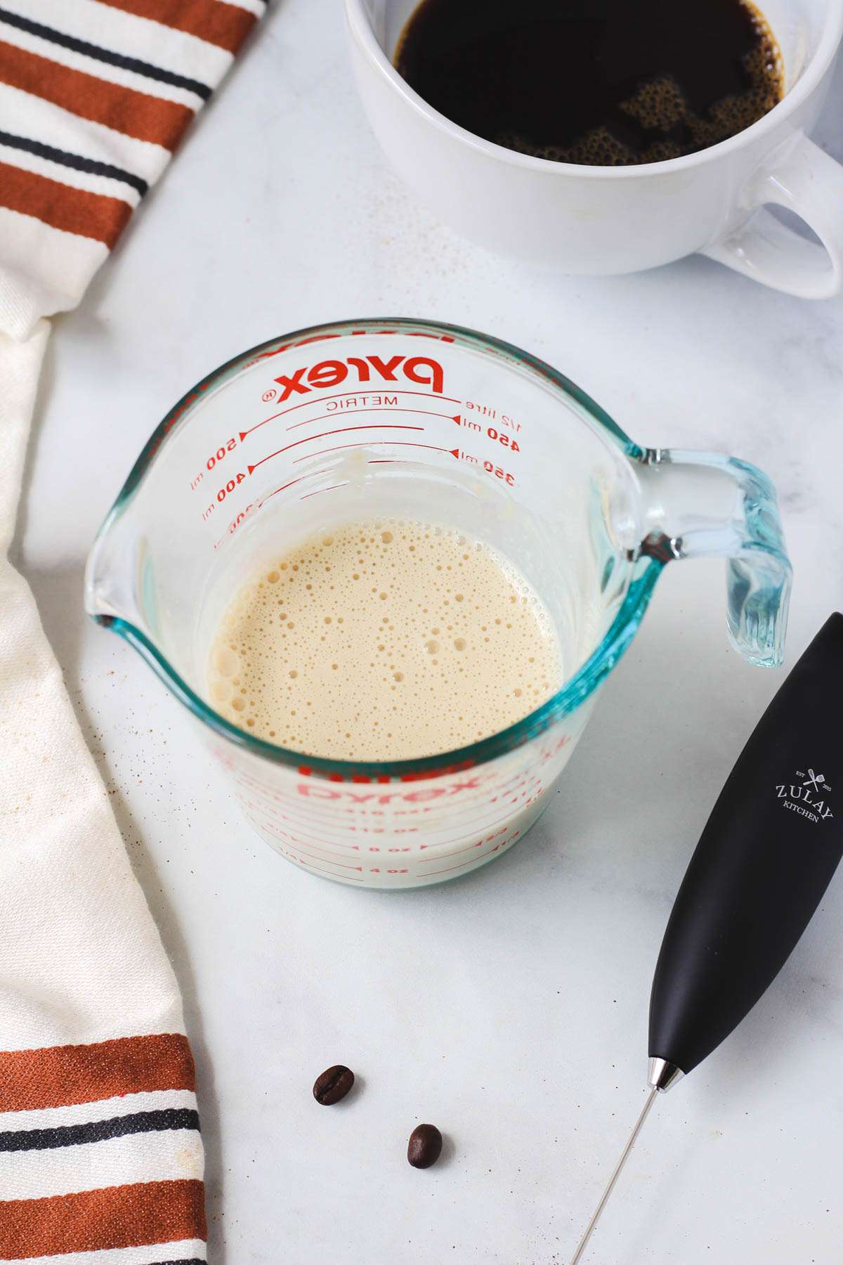 A liquid measuring cup with frothed vanilla protein oat milk.