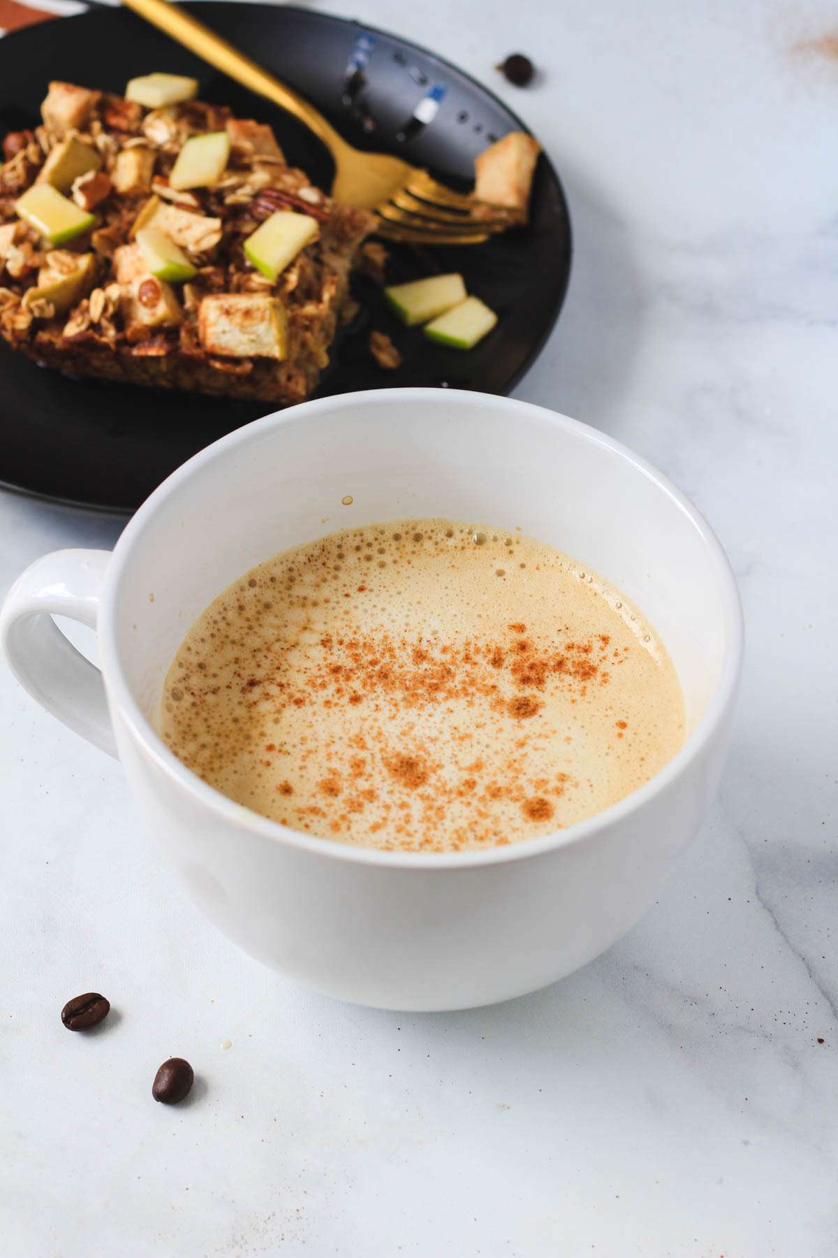 A large white mug with a vanilla protein coffee topped with ground cinnamon and an oatmeal square in the back.