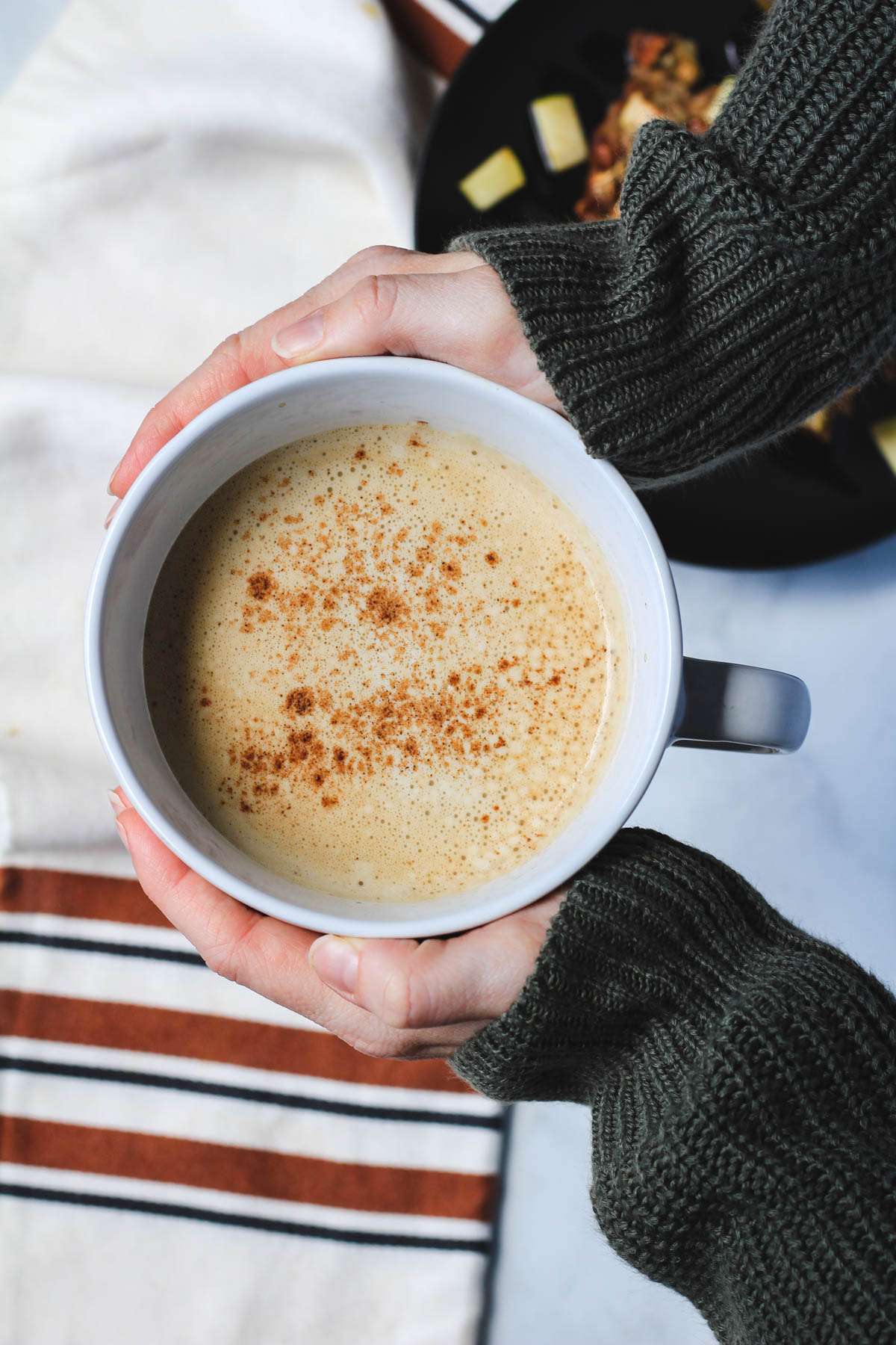 Two hands holding a cup of vegan vanilla proffee topped with fresh cinnamon.