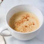 A white coffee mug filled with vegan vanilla proffee and topped with ground cinnamon.