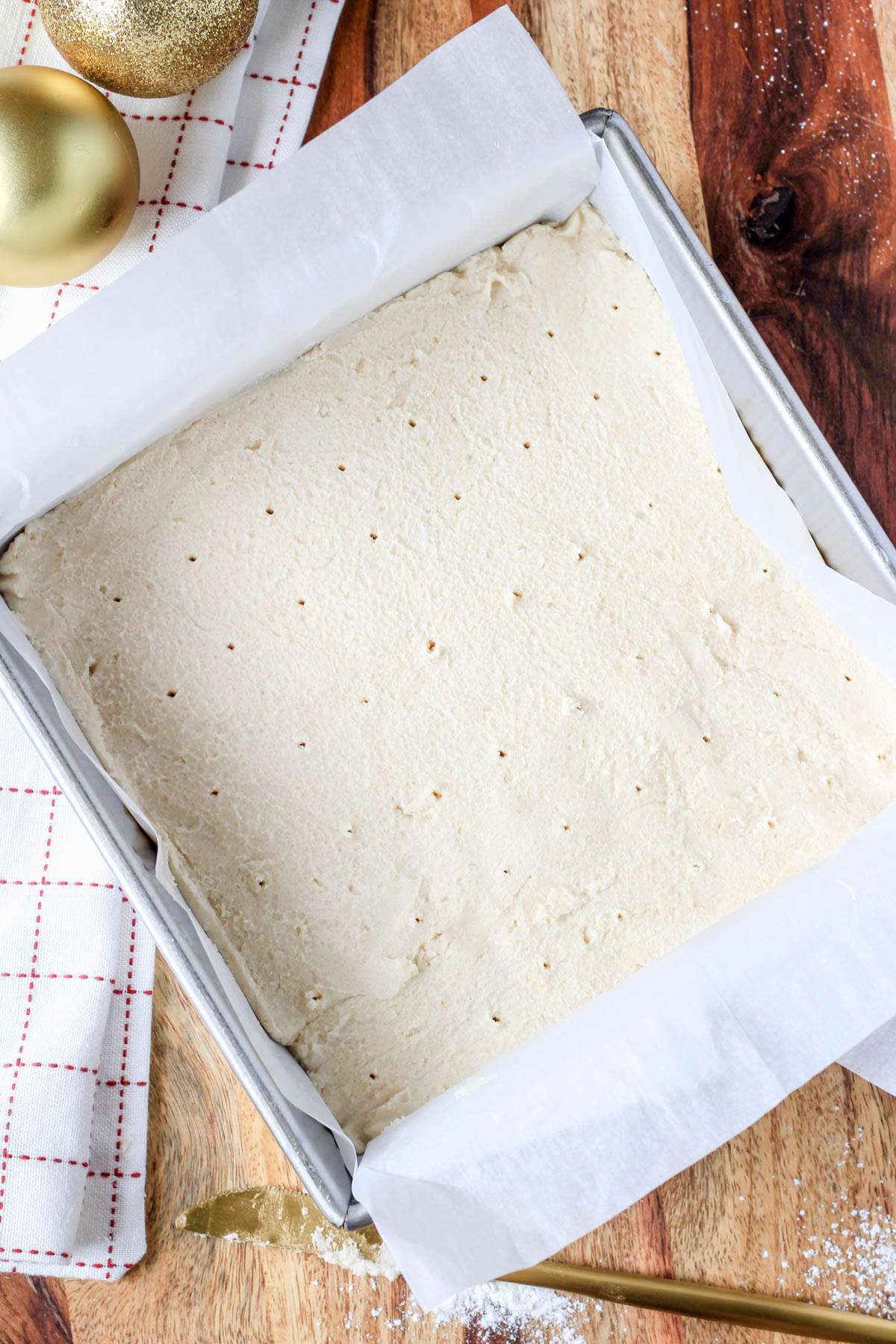 A lined baking dish on a wooden counter with vegan shortbread before baking.