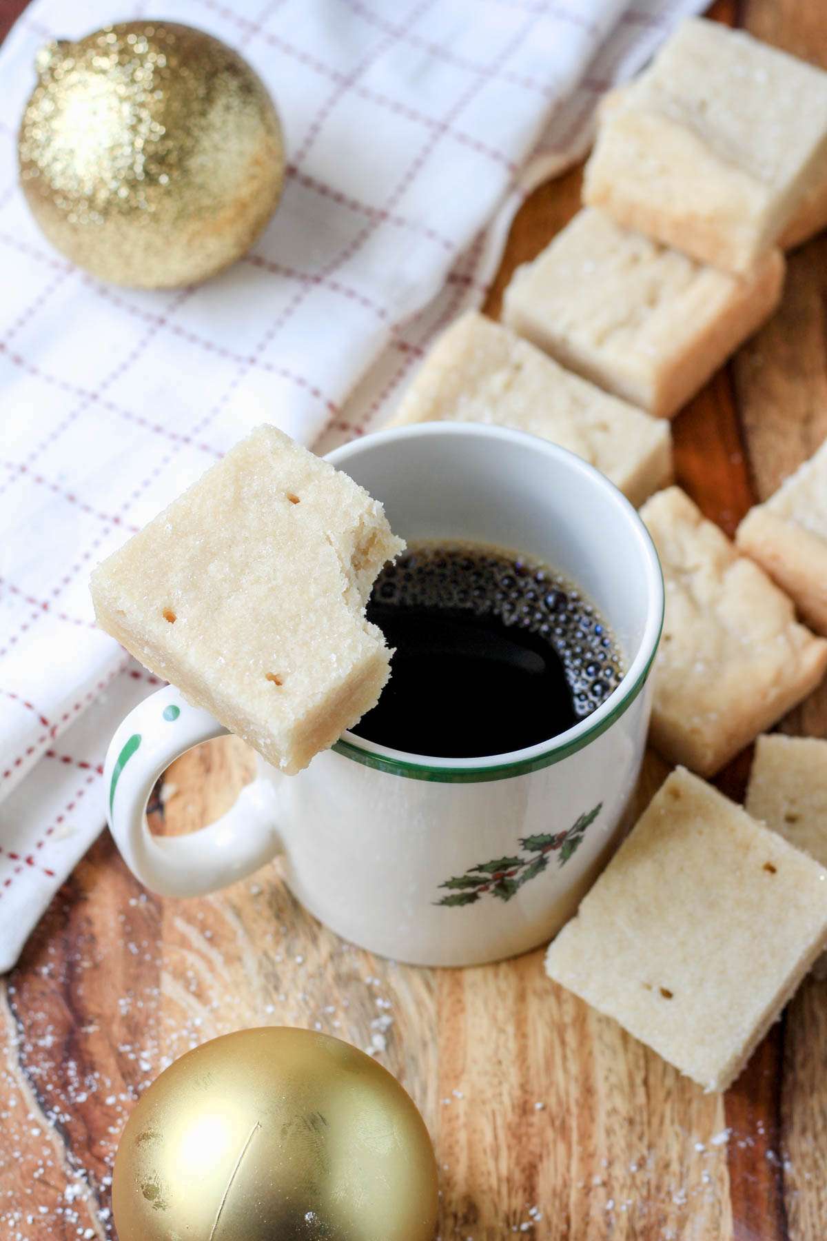 A cup of coffee on a wooden counter topped with a vegan shortbread cookie missing a bite.