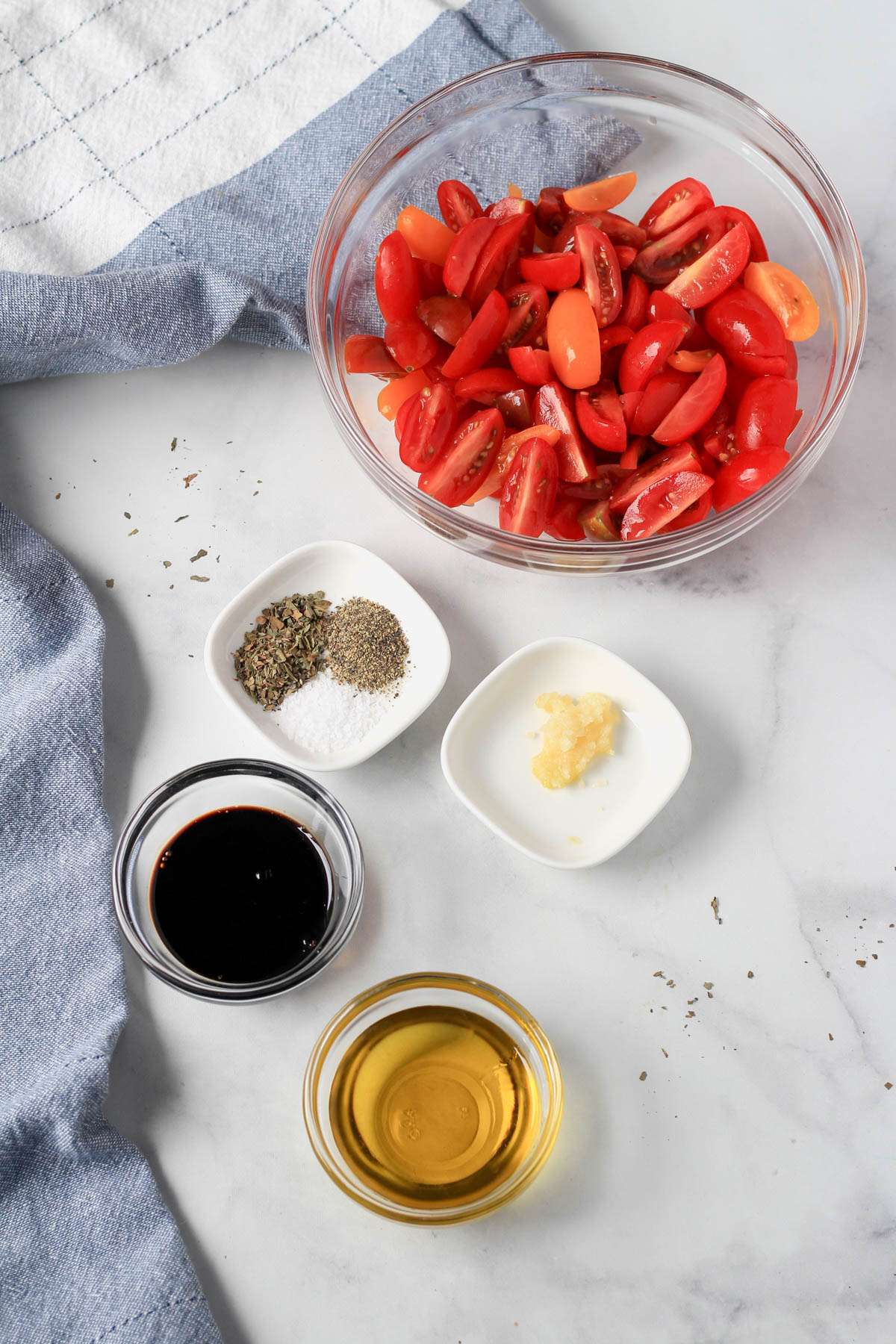 Ingredients for balsamic marinated tomatoes on a white counter with a blue and white towel to the left.
