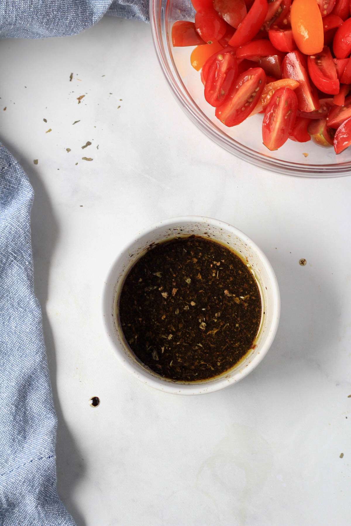 A white bowl with the balsamic marinade mixed together and a bowl of quartered tomatoes to the top right.