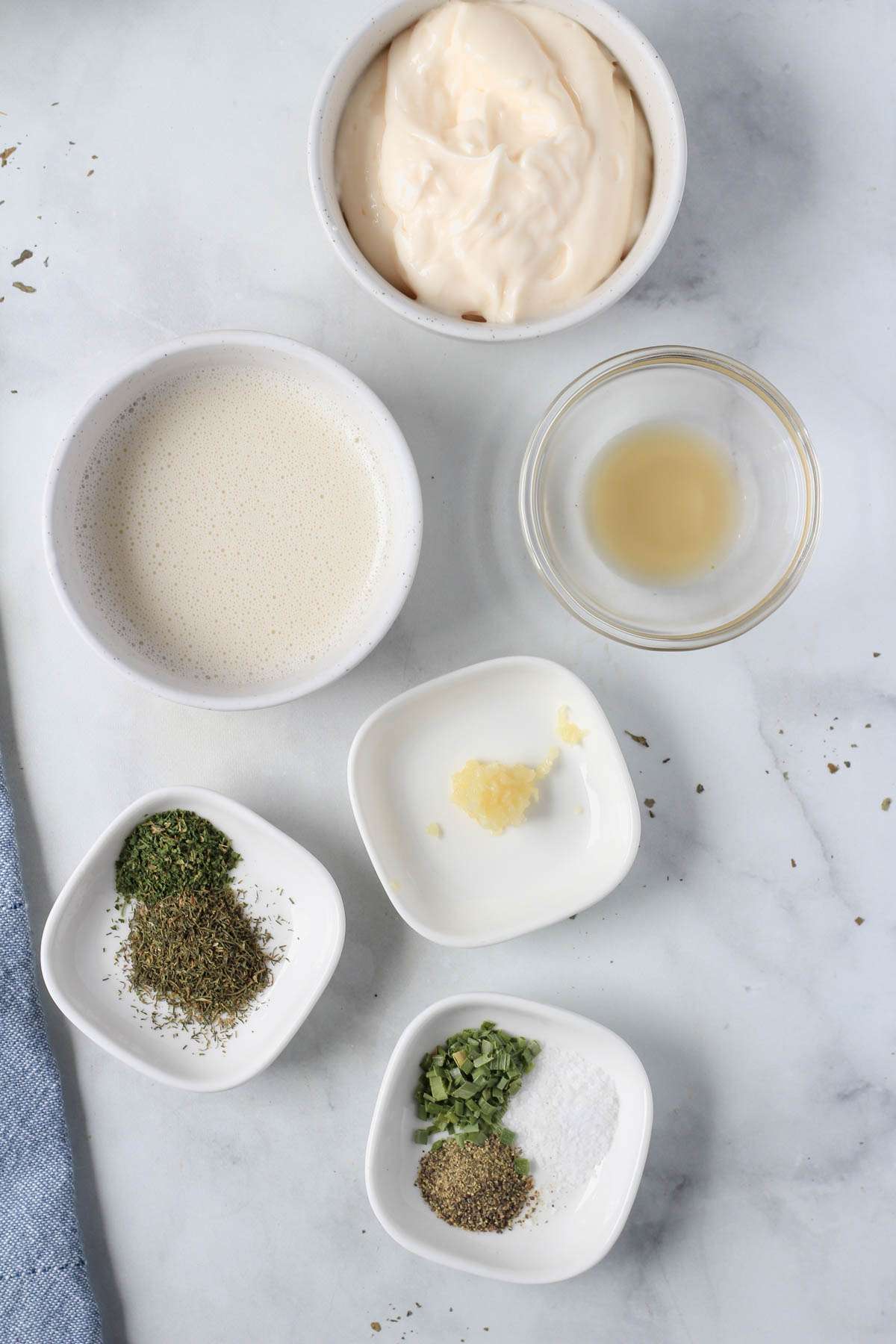 Ingredients for dairy-free ranch on a white counter with a blue towel on the left side.