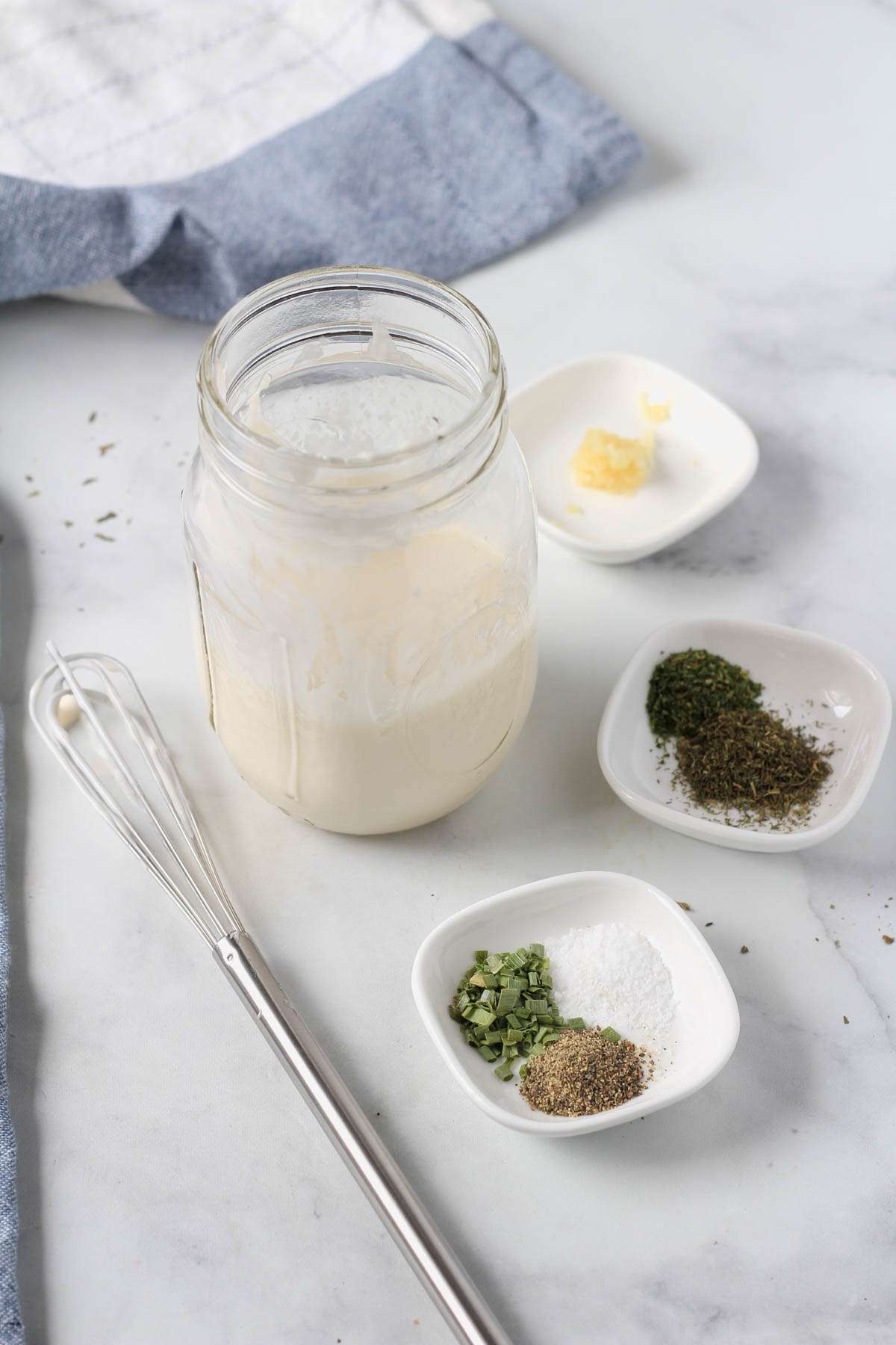 A mason jar with the wet ingredients for dairy-free ranch dressing and small white plates with the dry seasoning for the ranch.