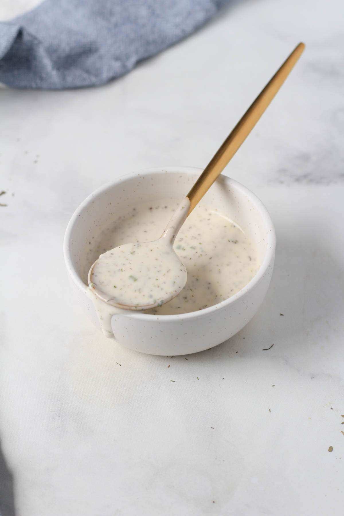 A white bowl with dairy-free ranch with a gold spoon on top.