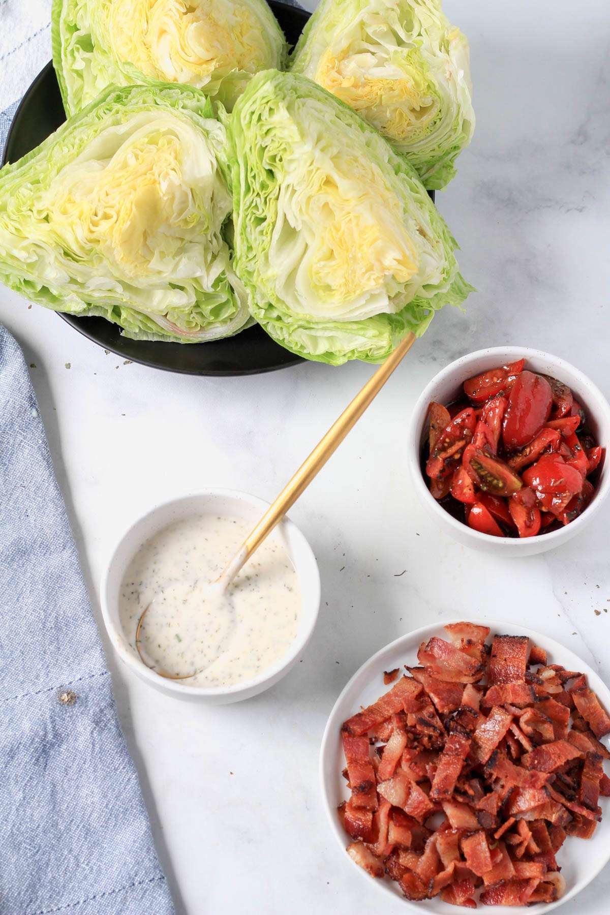 Ingredients for a dairy-free wedge salad on a white counter with a blue towel to the left.