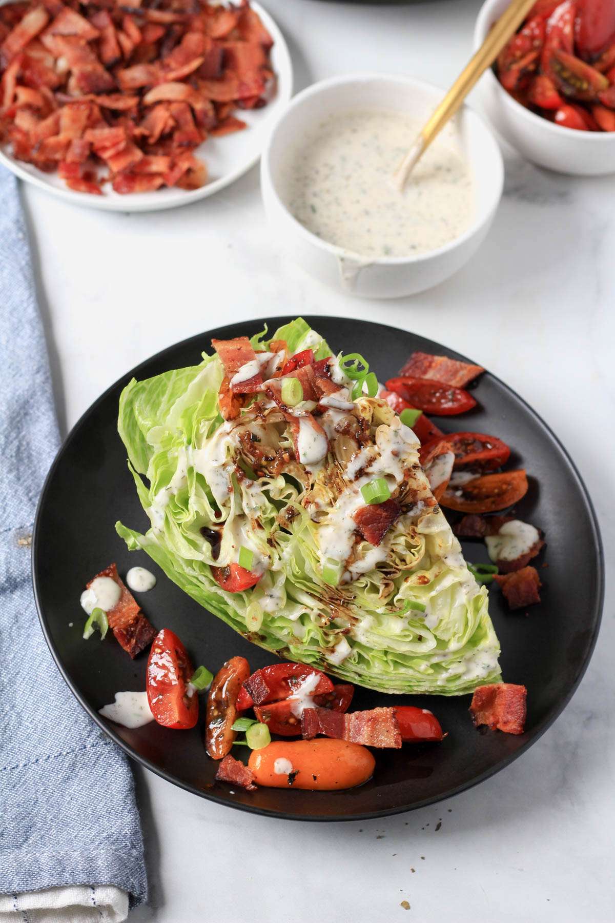 A black plate with a dairy-free wedge salad with toppings in the back.