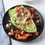 A black plate with a dairy-free wedge salad topped with ranch, tomatoes, bacon, and green onion.