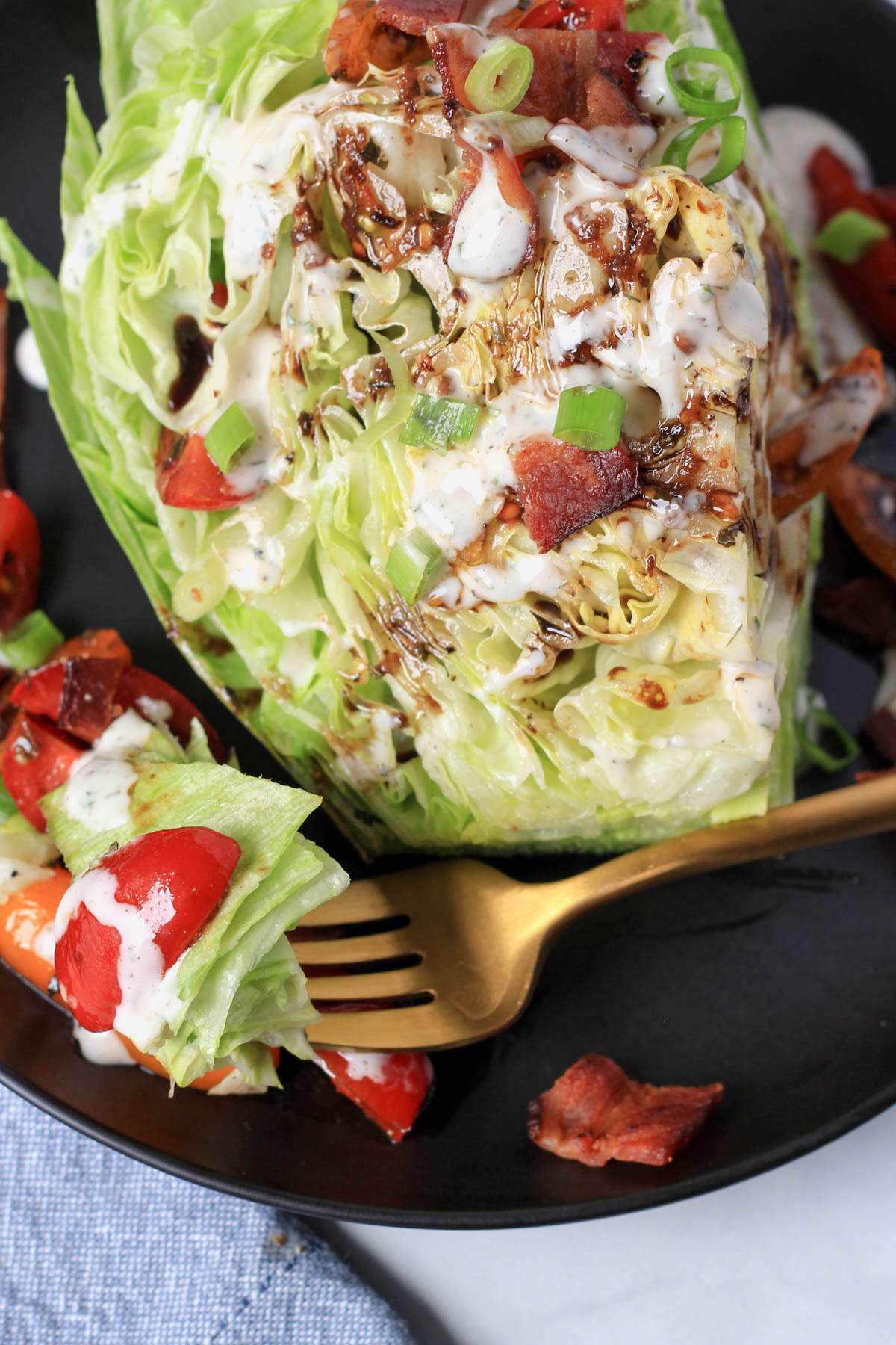 A fork with a bite of wedge salad on a black plate.