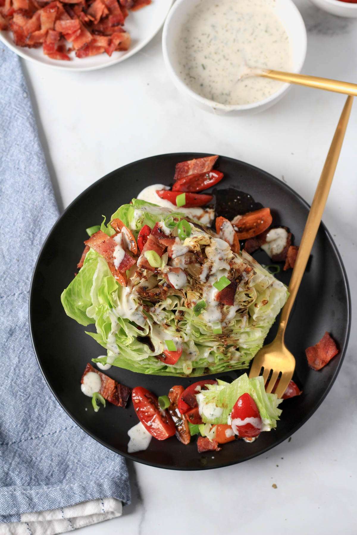 A top down photo of a dairy-free wedge salad topped with bacon, tomato, and dairy-free ranch with a fork in the front.