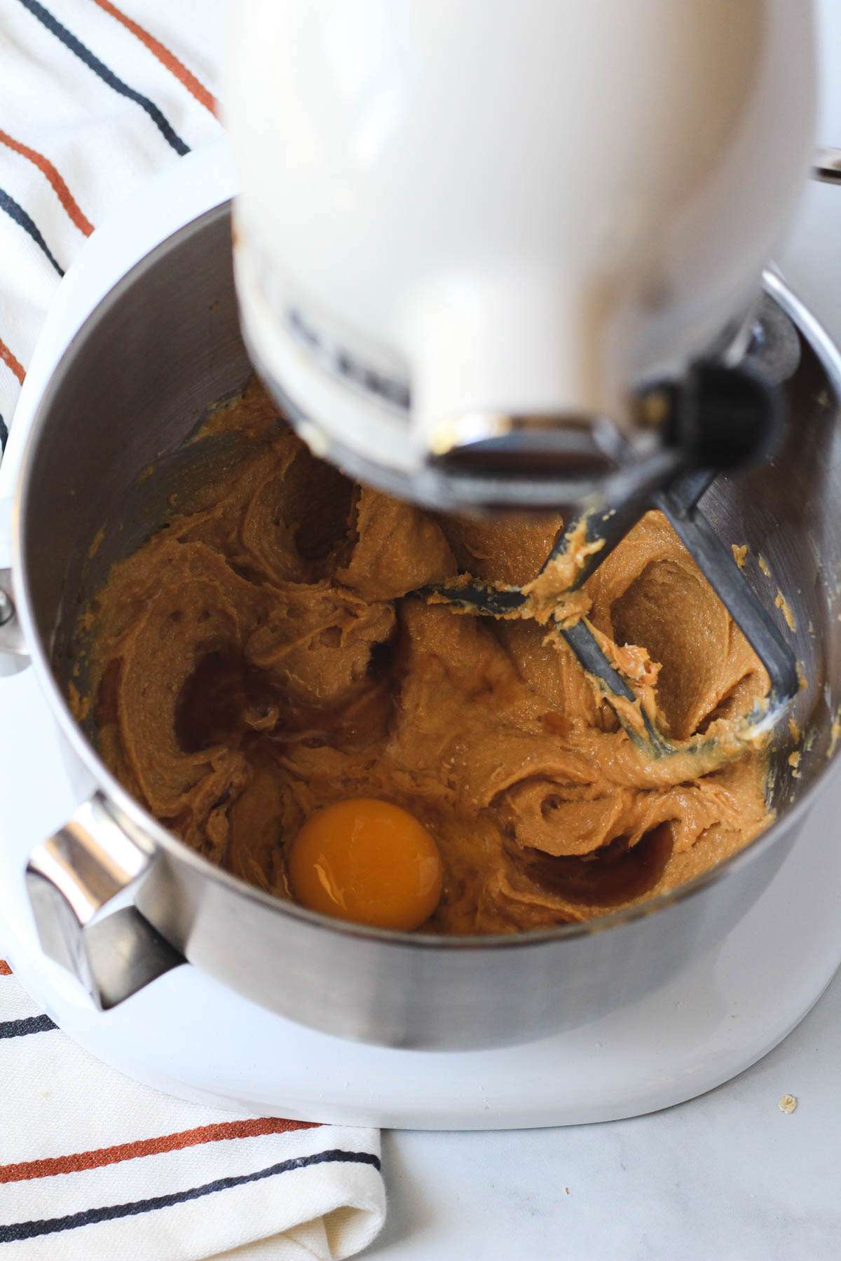 A silver mixing bowl with creamed peanut butter mixture topped with an egg and vanilla.