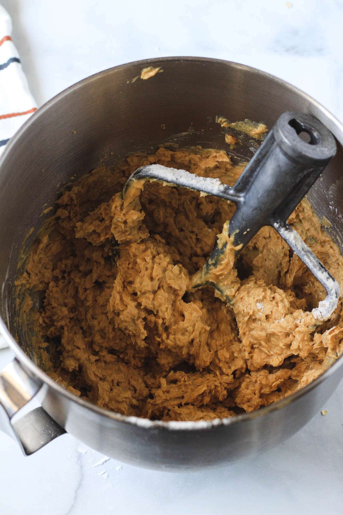 A silver mixing bowl with the paddle attachment and peanut butter oatmeal cookie dough in the bowl.