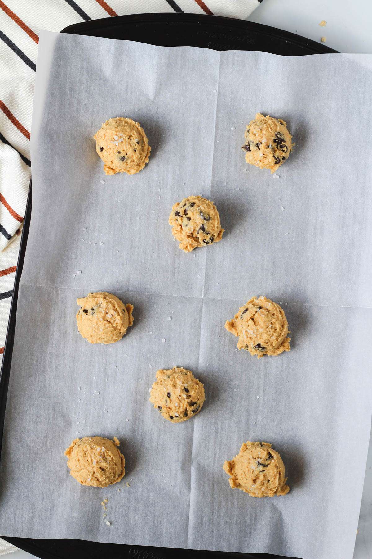 A baking sheet lined with parchment paper topped with peanut butter chocolate chip oatmeal cookies sprinkled with flaky sea salt.