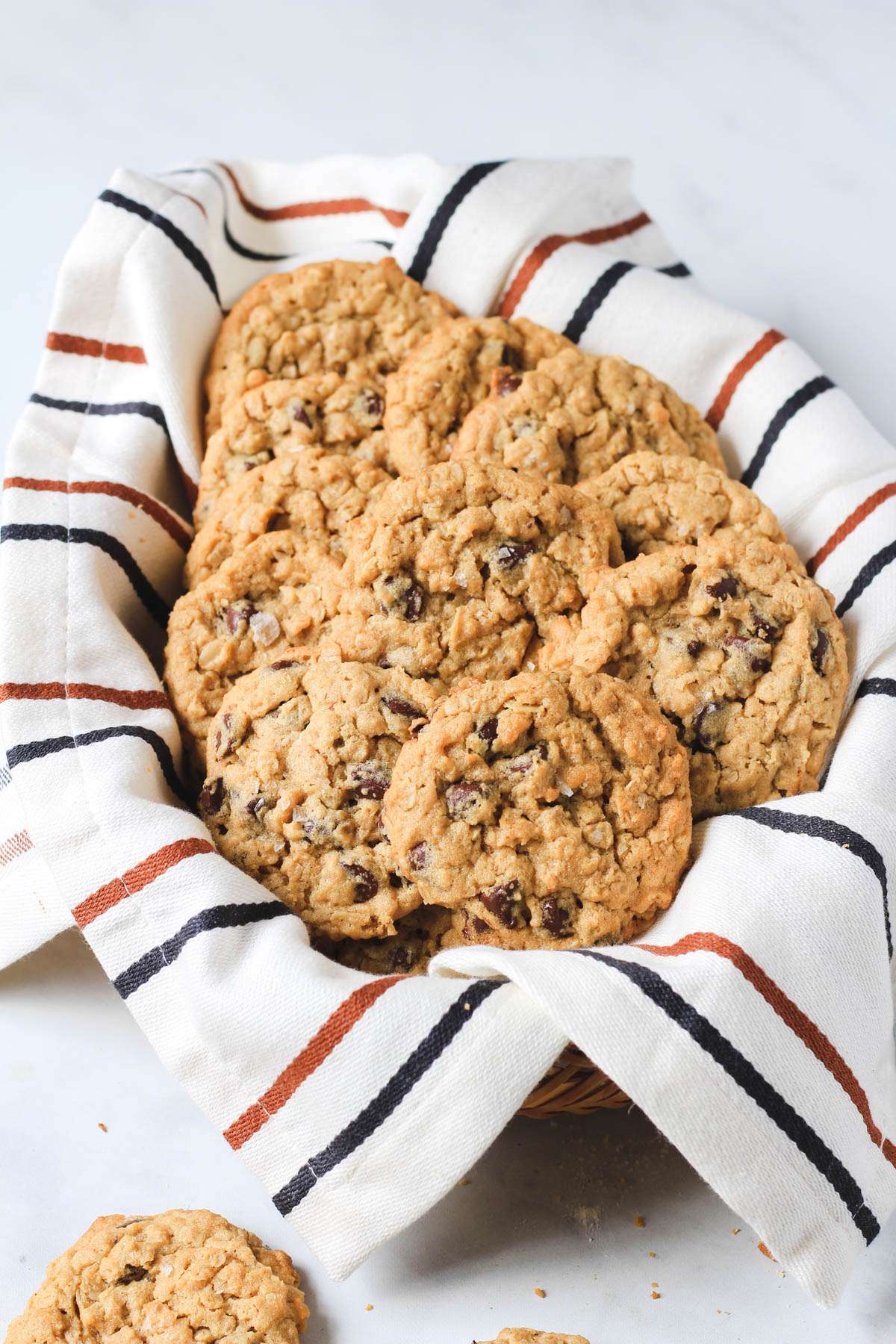 A basket lined with a dish towel and filled with peanut butter chocolate chip oatmeal cookies.