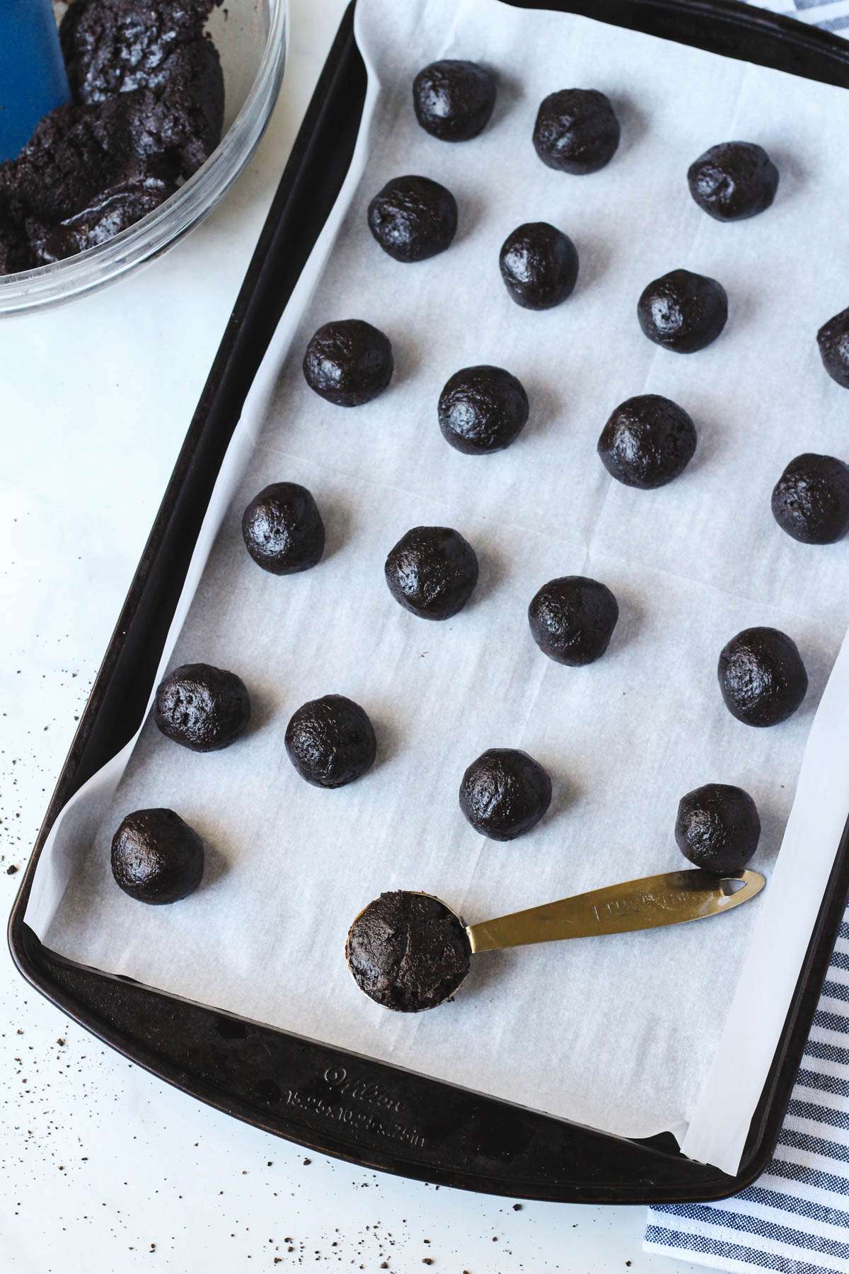 A rimmed baking sheet with parchment paper and scoops of oreo truffle balls before they freeze.