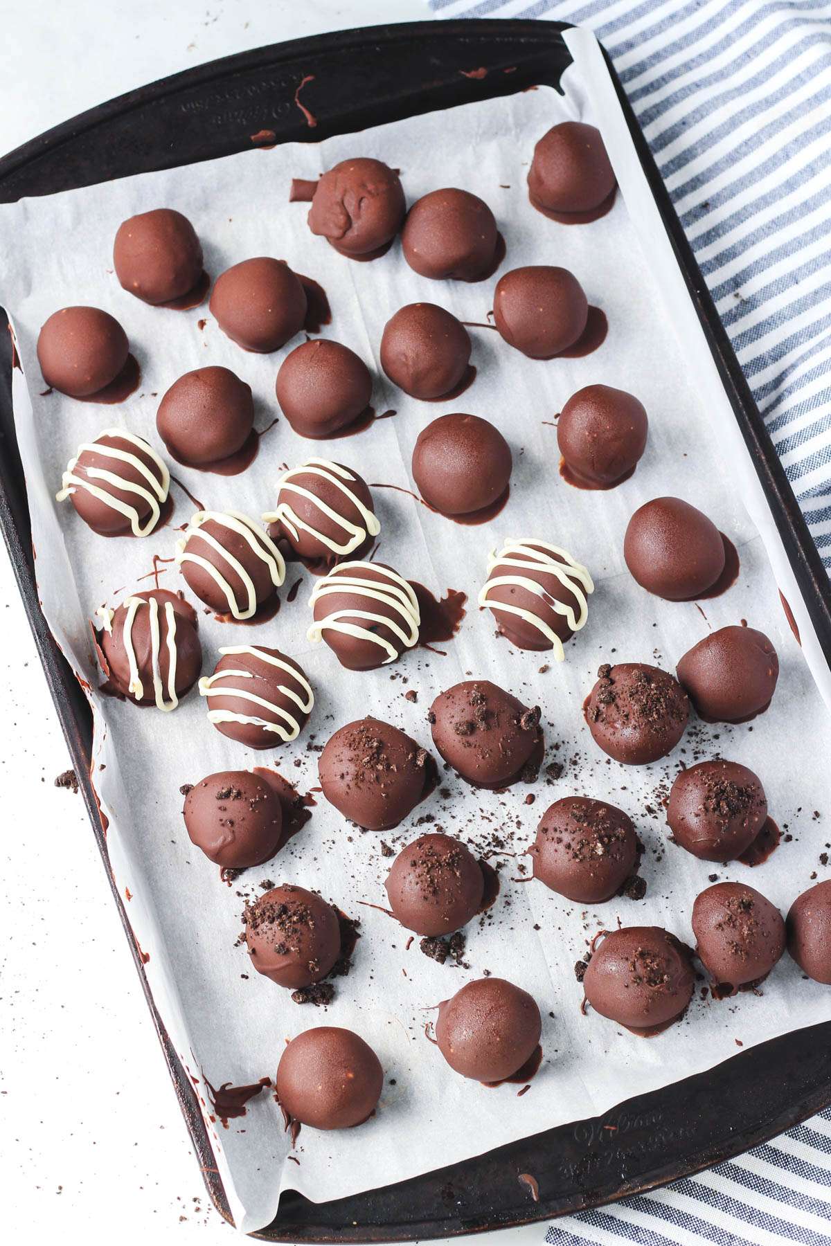 A rimmed baking sheet lined with parchment paper and topped with decorated Oreo truffle balls.