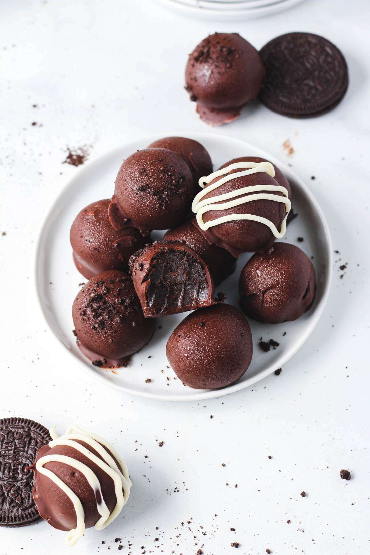 A small white plate filled with vegan oreo truffle balls on a white counter with two oreos in the right and left corners.