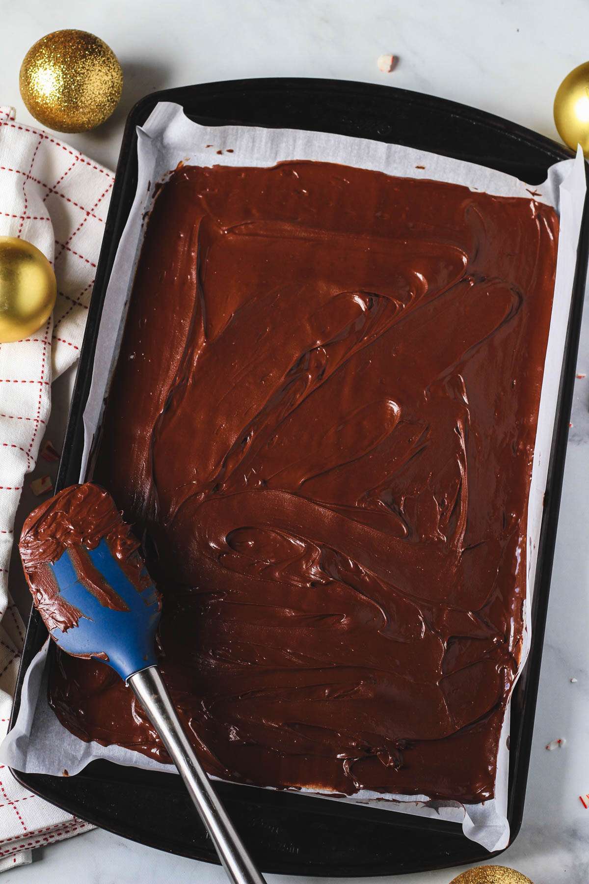 A rimmed baking sheet with the chocolate layer of peppermint bark spread out.
