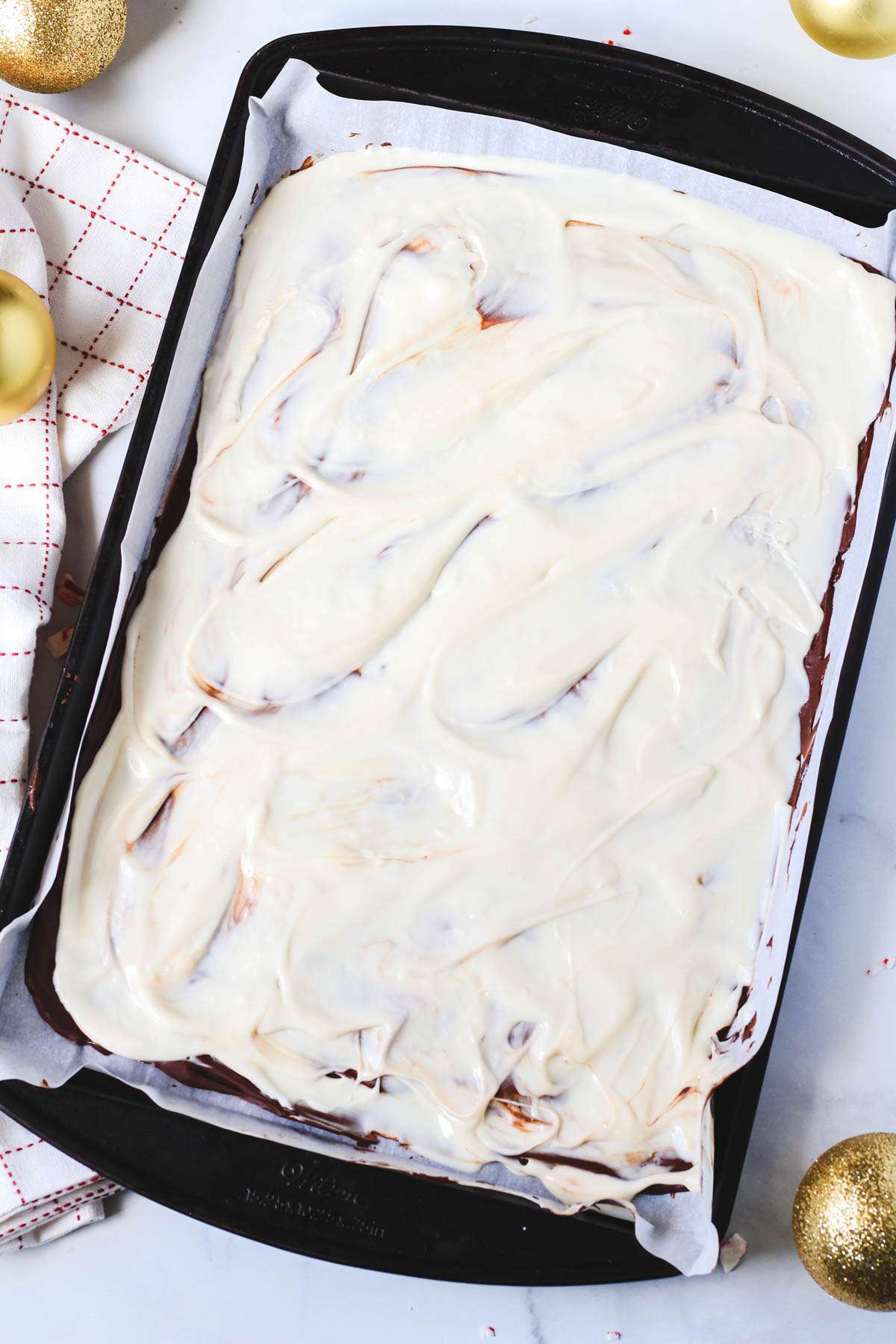 A rimmed baking sheet with the white chocolate layer of peppermint spread on top of the chocolate layer.