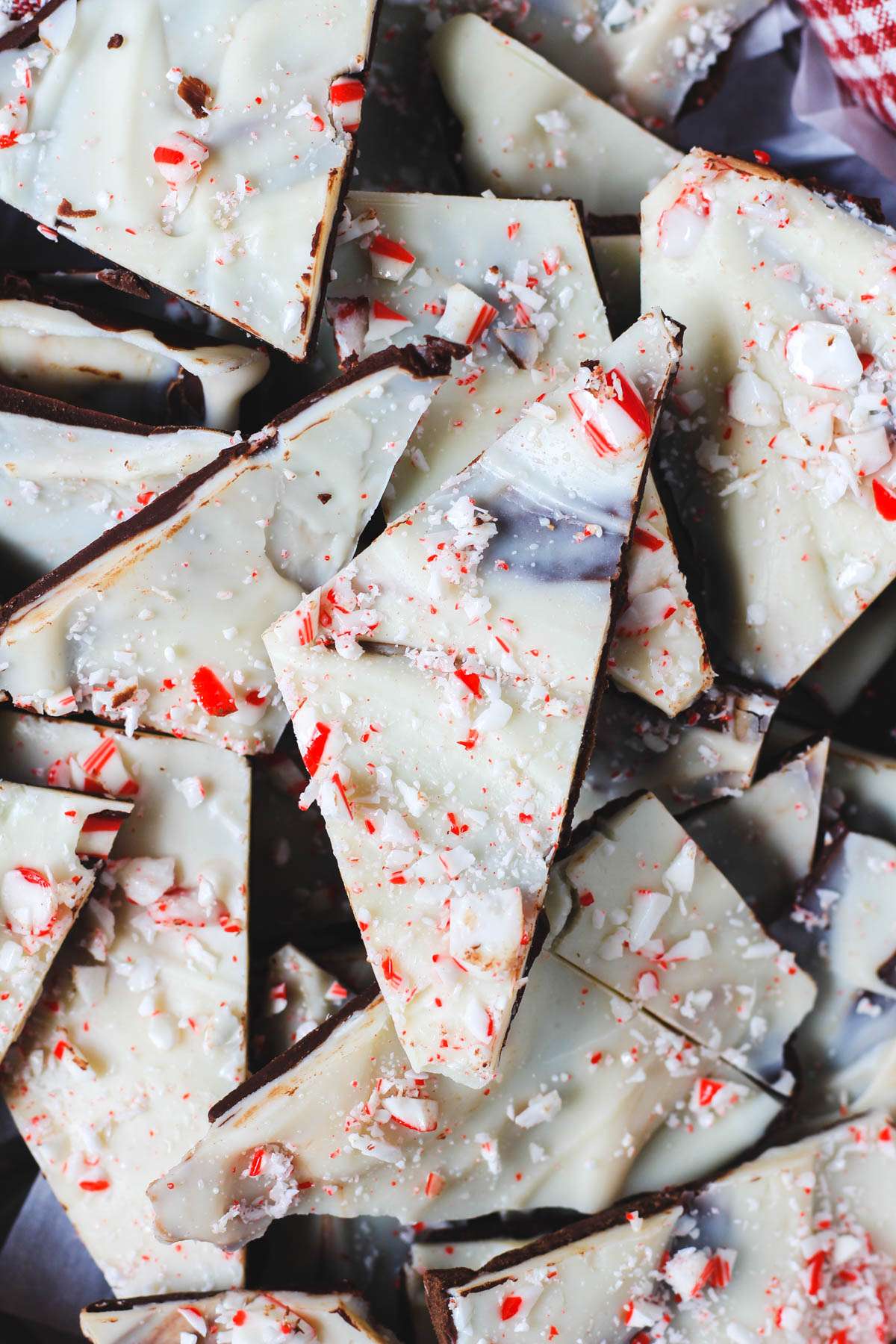 A triangular shaped piece of peppermint bark on a pile of vegan peppermint bark.