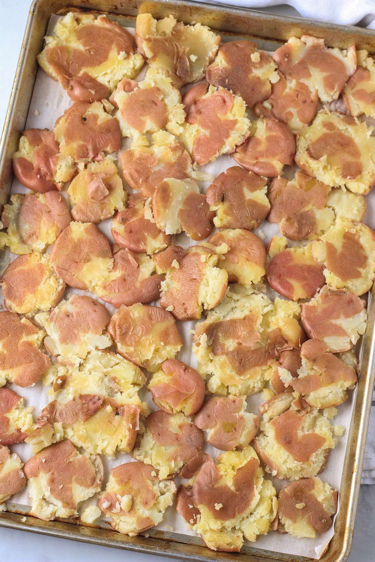 A rimmed baking sheet topped with smashed potatoes.