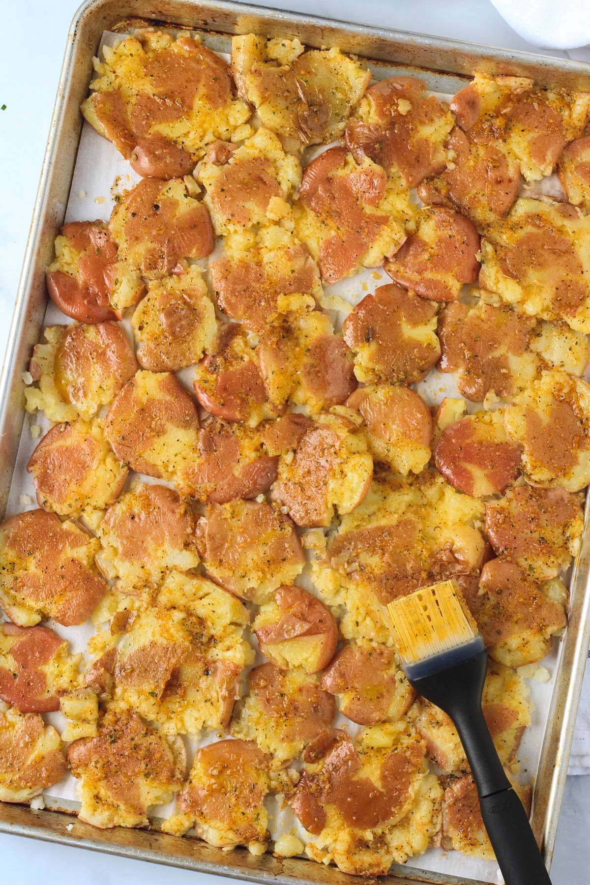 A rimmed baking sheet with smashed potatoes after being brushed with the olive oil mixture.
