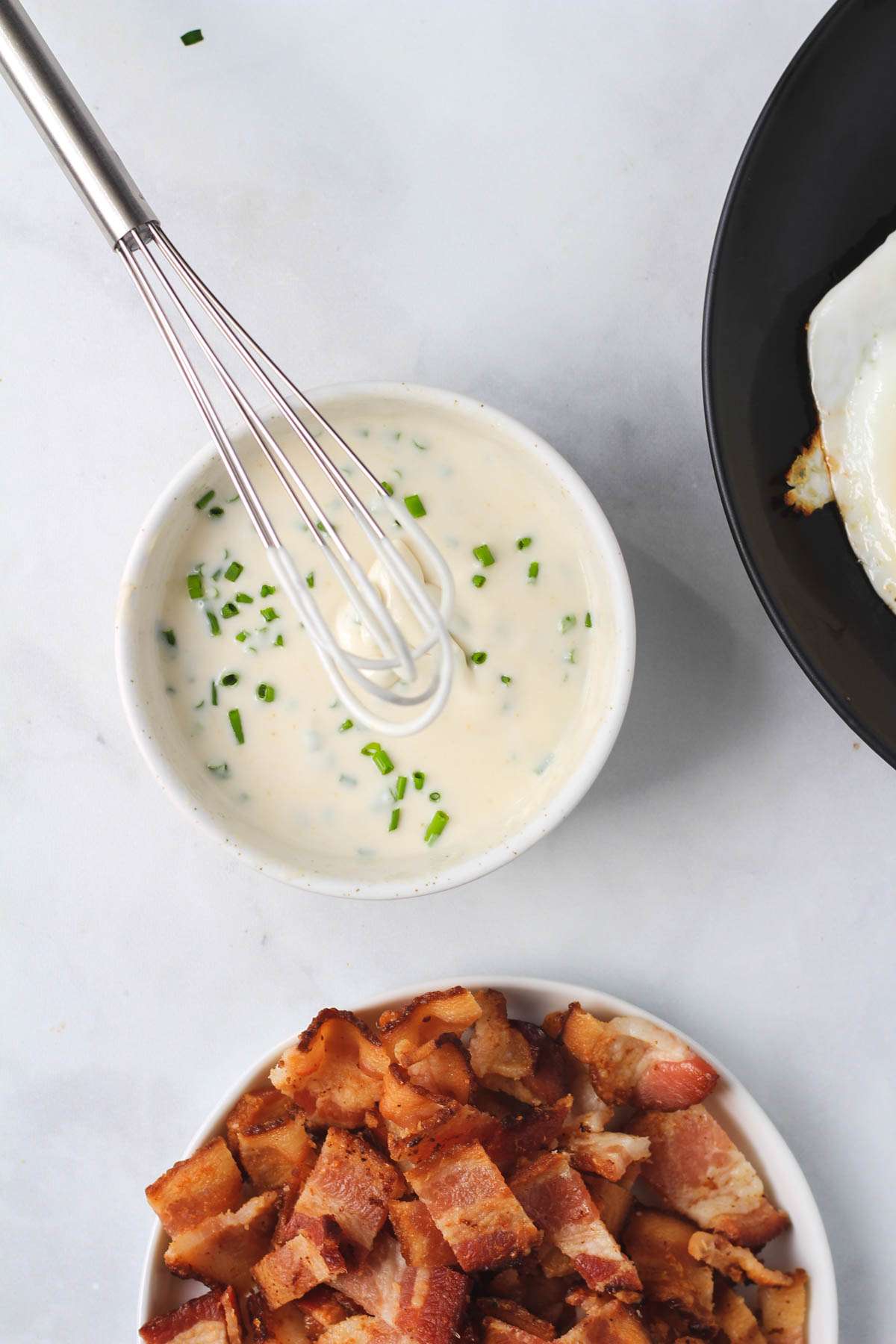 A white bowl with chive sour cream and a small whisk.