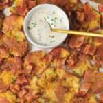 A close up of the white bowl of chive sour cream with a gold spoon surrounded by breakfast smashed potatoes.