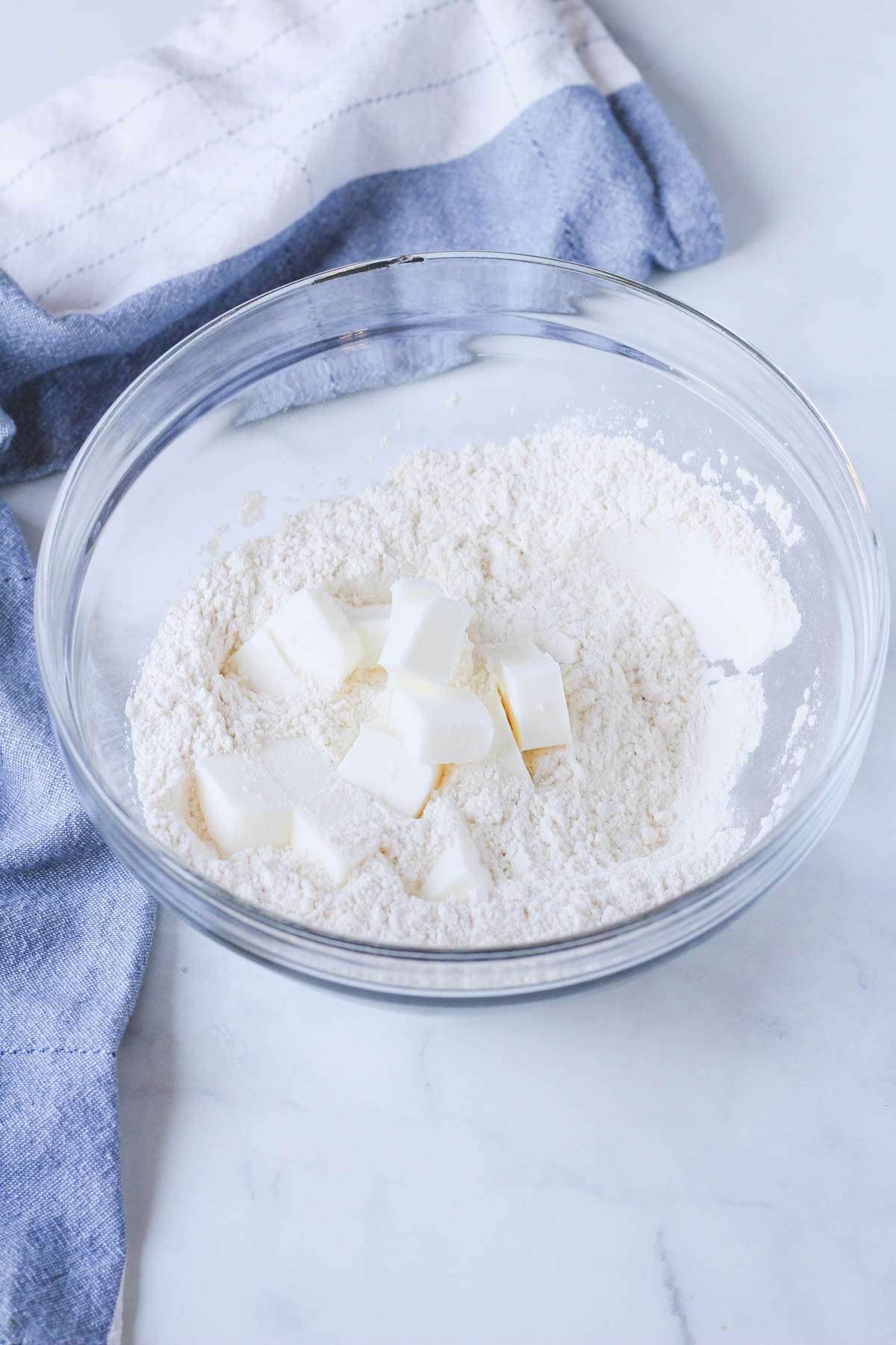 A glass mixing bowl with shortening on top of a flour and salt mixture.