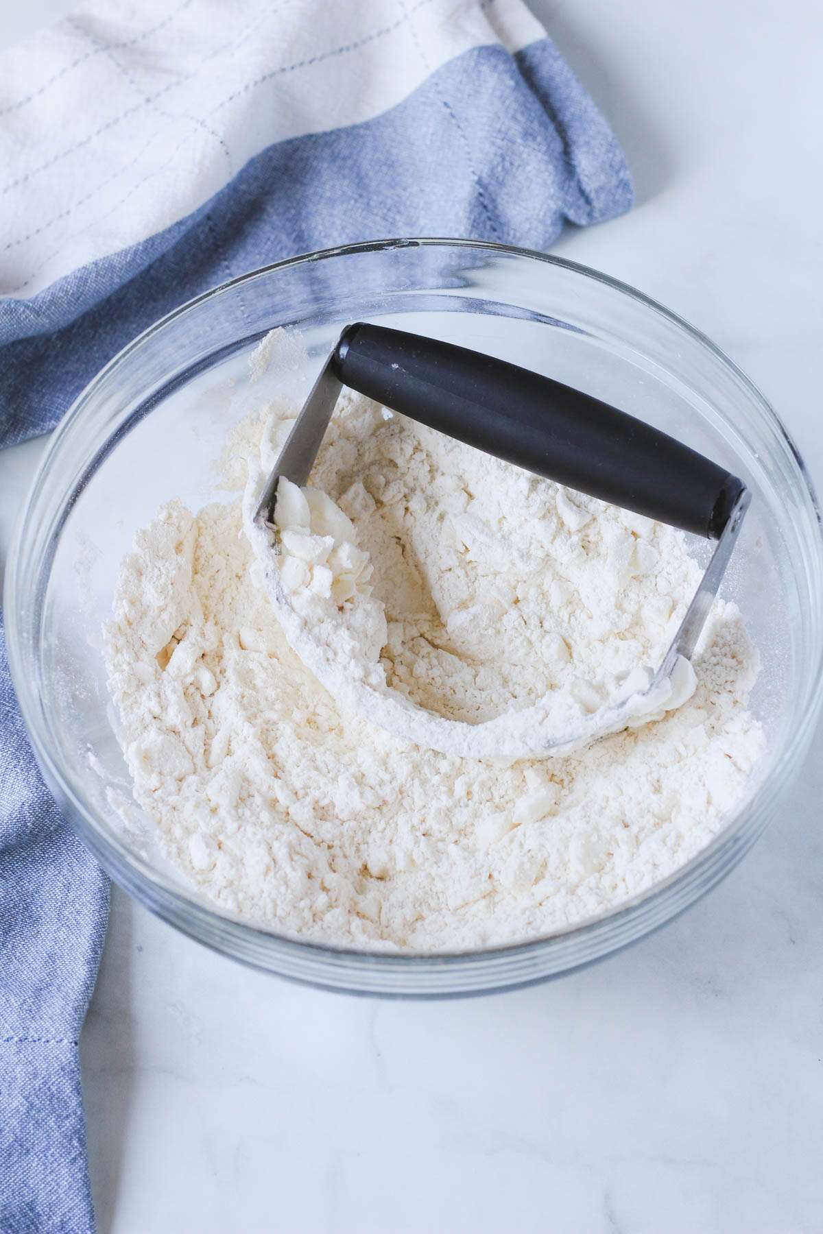 A glass bowl with a pastry blender cutting shortening into the flour and salt mixture.
