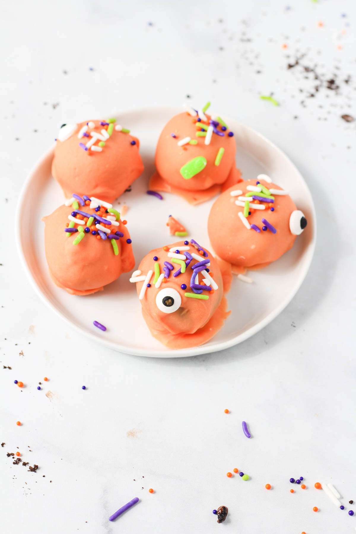 A white plate with orange coated Oreo truffles topped with sprinkles and candy eyes.