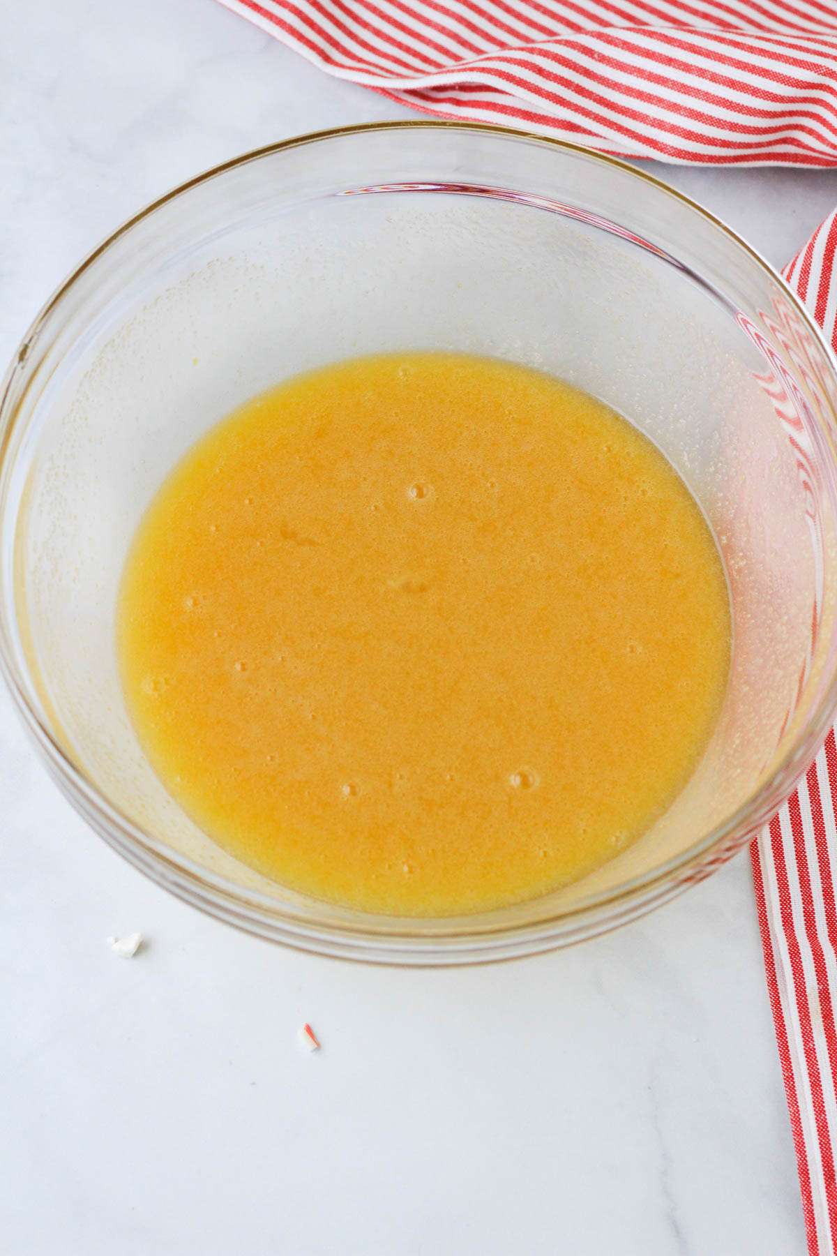 A glass mixing bowl with the wet ingredients combined on a white counter.