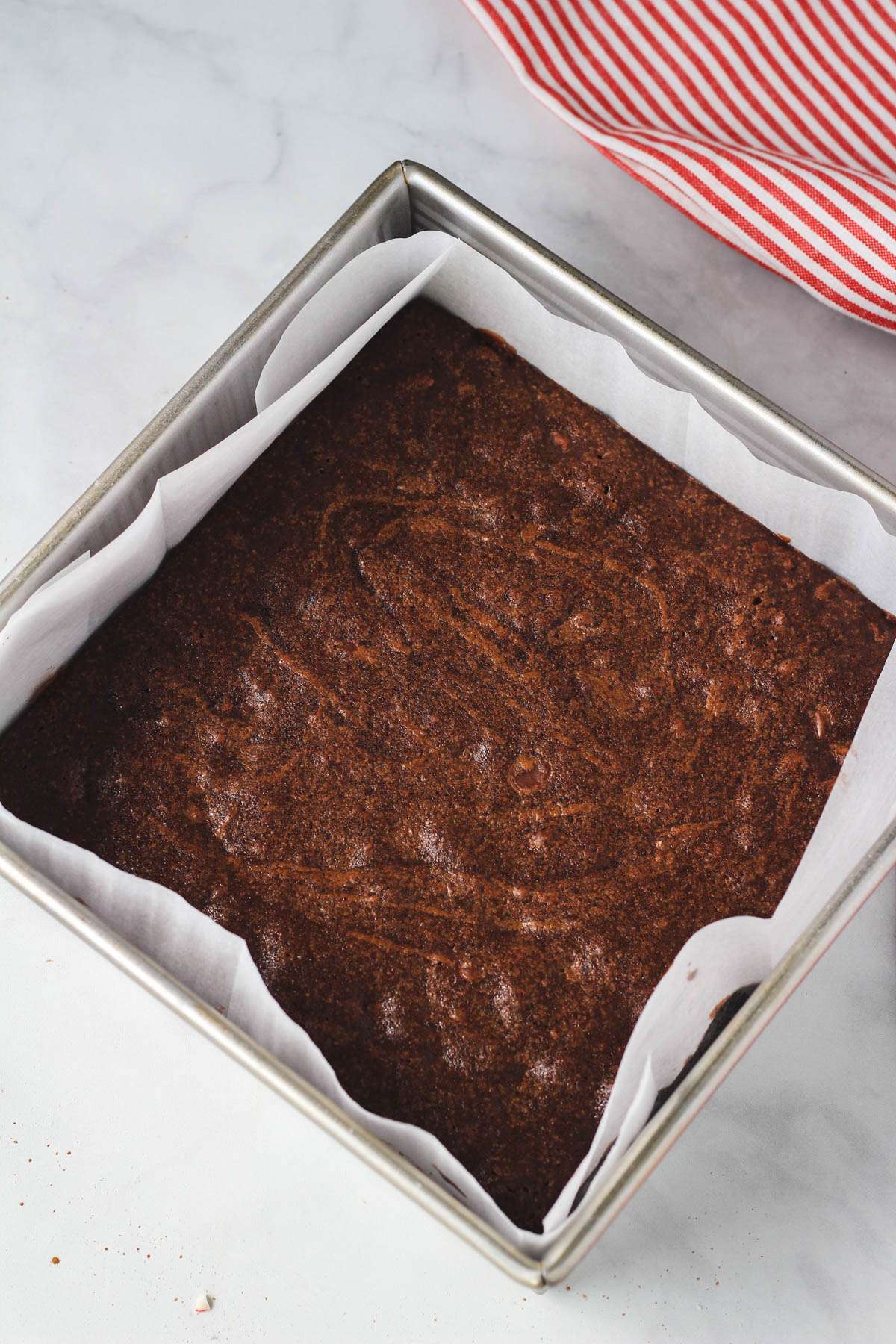 A square baking pan lined with parchment paper and filled with baked peppermint brownies.