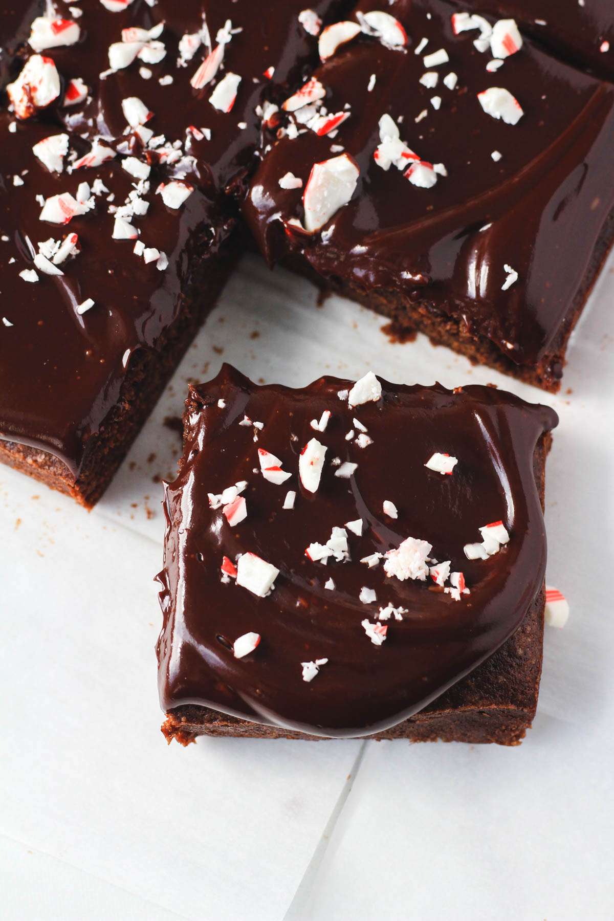 A peppermint brownie topped with crushed peppermint pulled away from the rest of the sliced brownies on a piece of parchment paper.