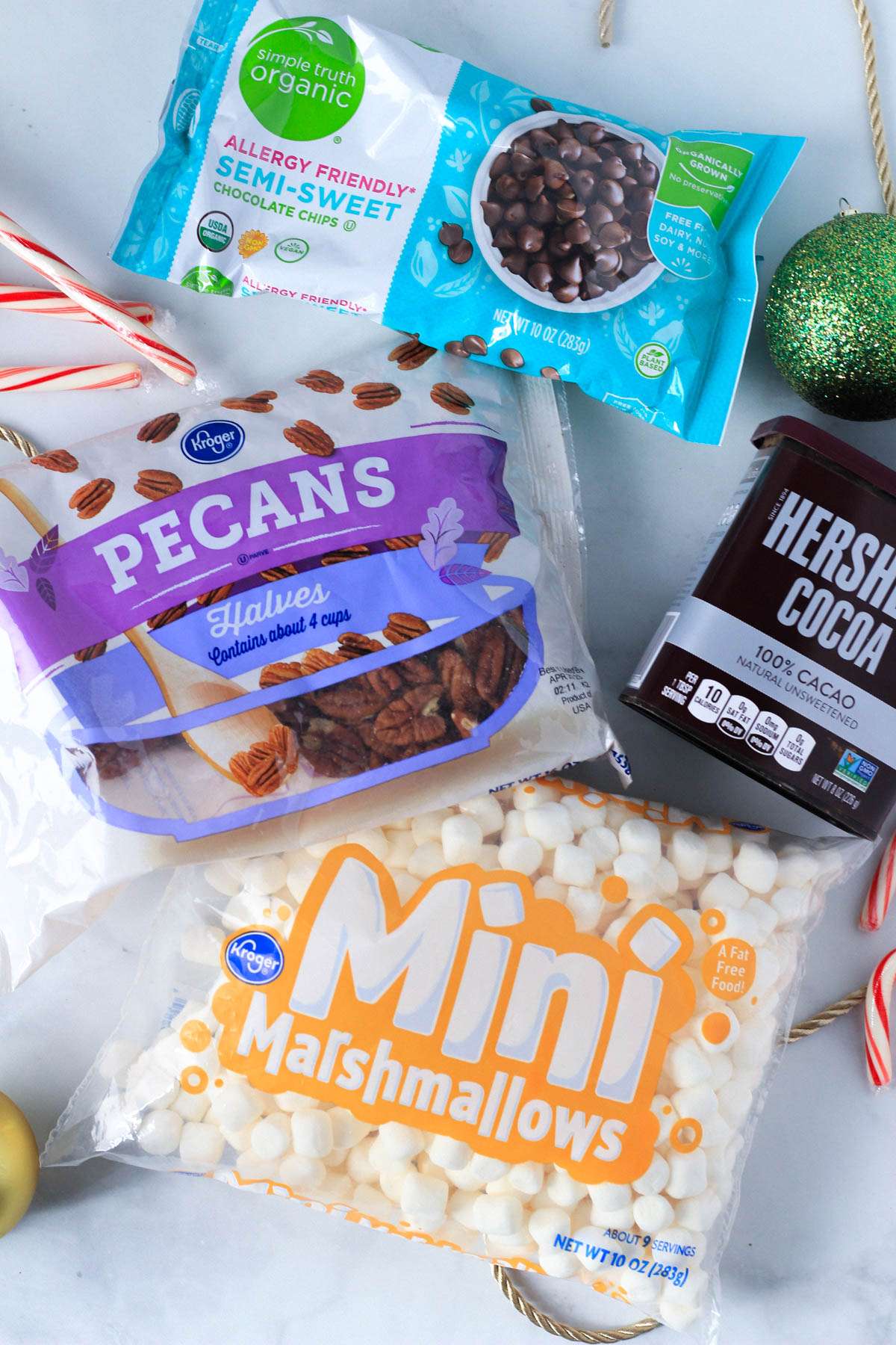 Chocolate chips, pecans, marshmallows, and cocoa powder on a white counter with candy canes around.