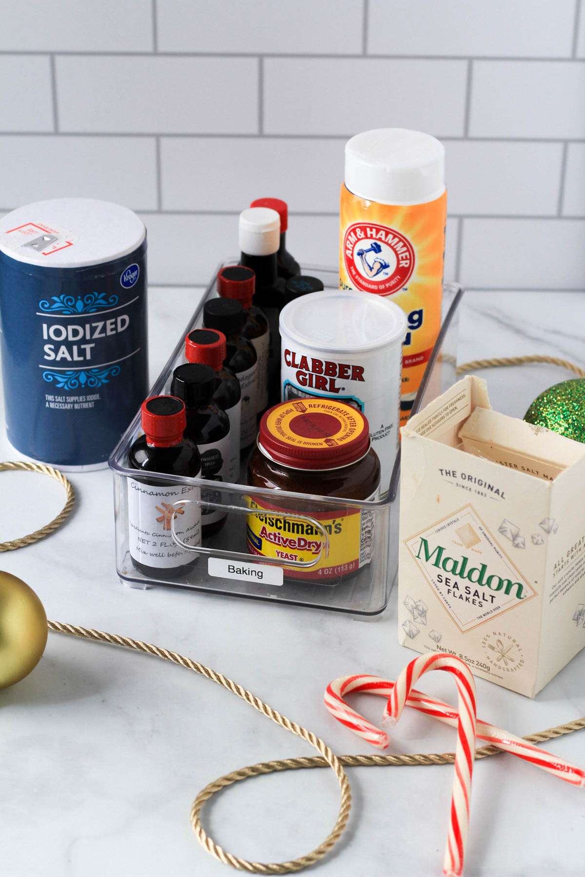 Baking ingredients like salt, extracts, yeast, baking soda, and baking powder on a white counter with a tile background.